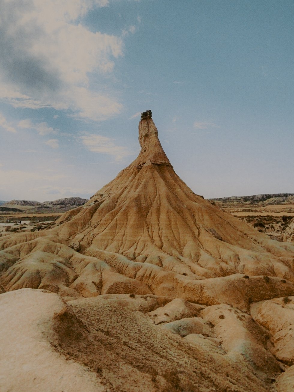 Paysage désertique avec une formation rocheuse en forme de colline pointue sous un ciel partiellement nuageux.