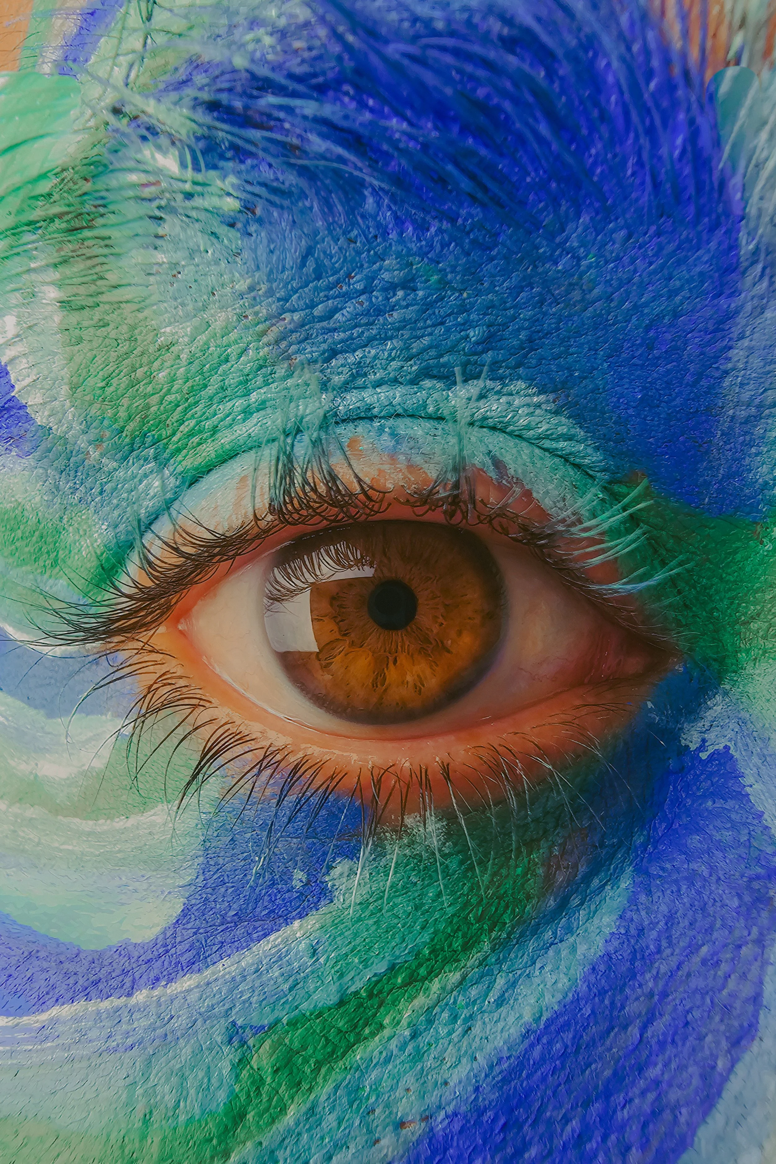Un œil humain avec une iris marron entouré de peinture en couleur verte, bleue et orange.