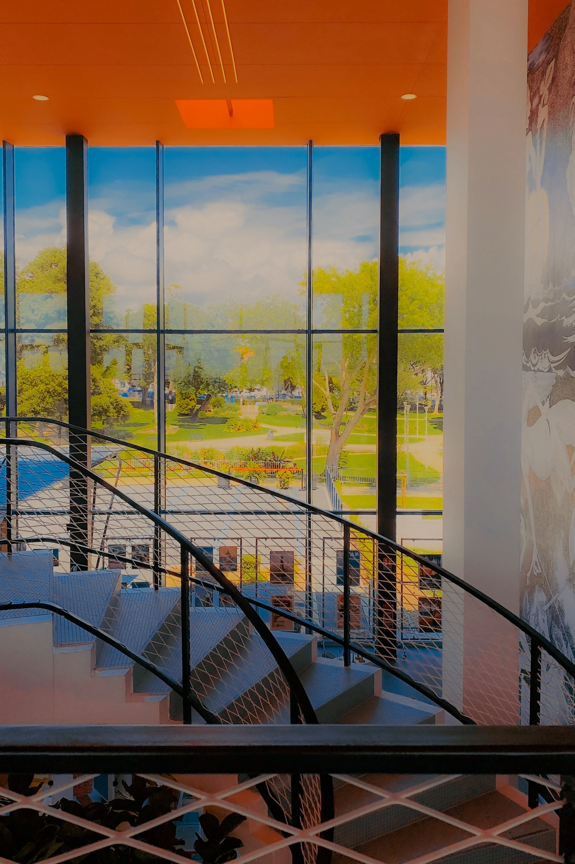 Intérieur moderne avec un escalier en spirale en métal noir, grandes fenêtres donnant sur un espace vert extérieur et mur décoratif avec motifs.