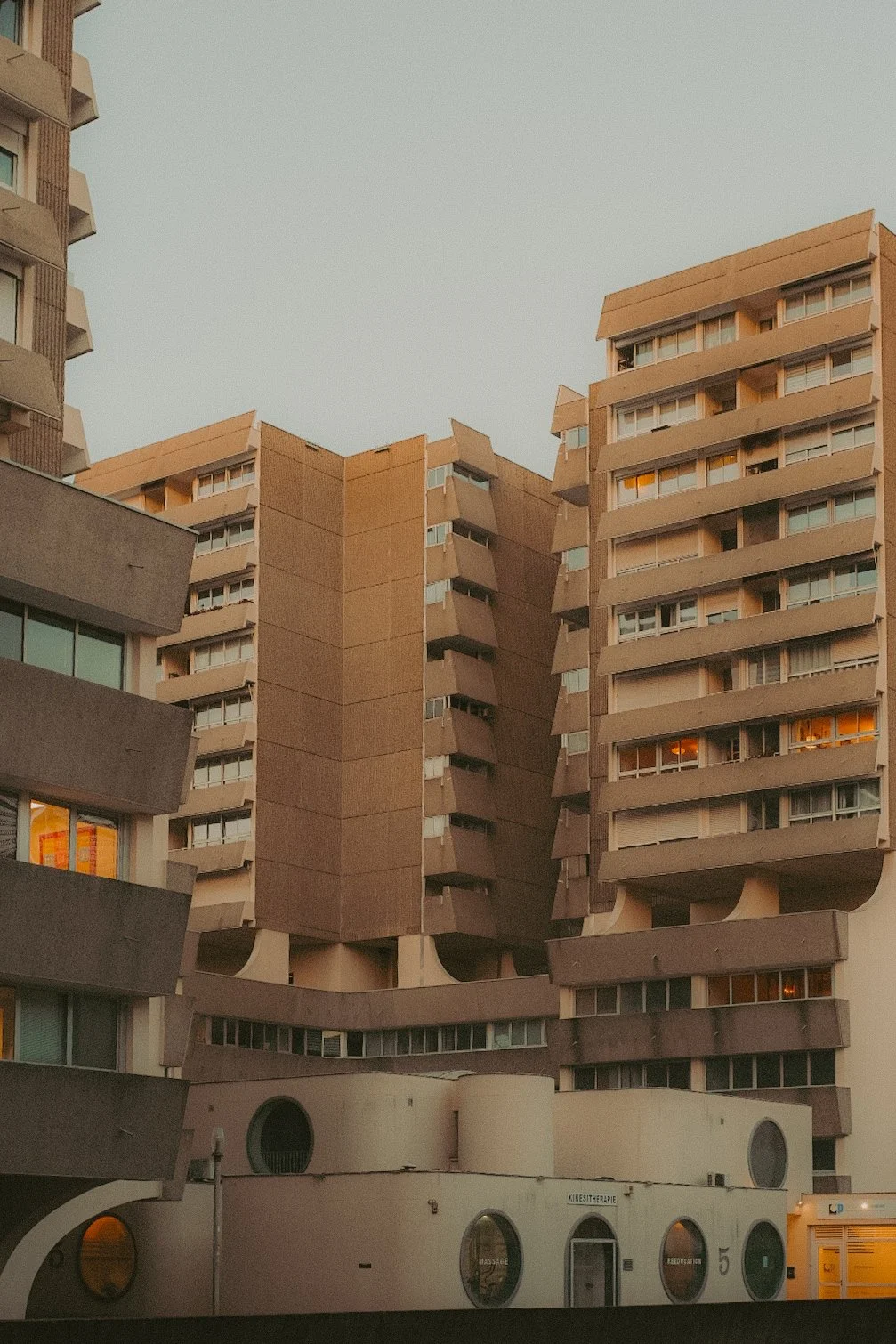 Un immeuble résidentiel en béton avec plusieurs étages et balcons, architecture moderniste, éclairage chaud dans certaines fenêtres, structure complexe avec formes arrondies et angularités.