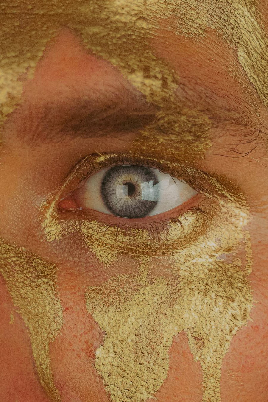 Un œil humain avec un maquillage doré autour de l'œil, y compris la paupière, les cils, et la peau environnante.