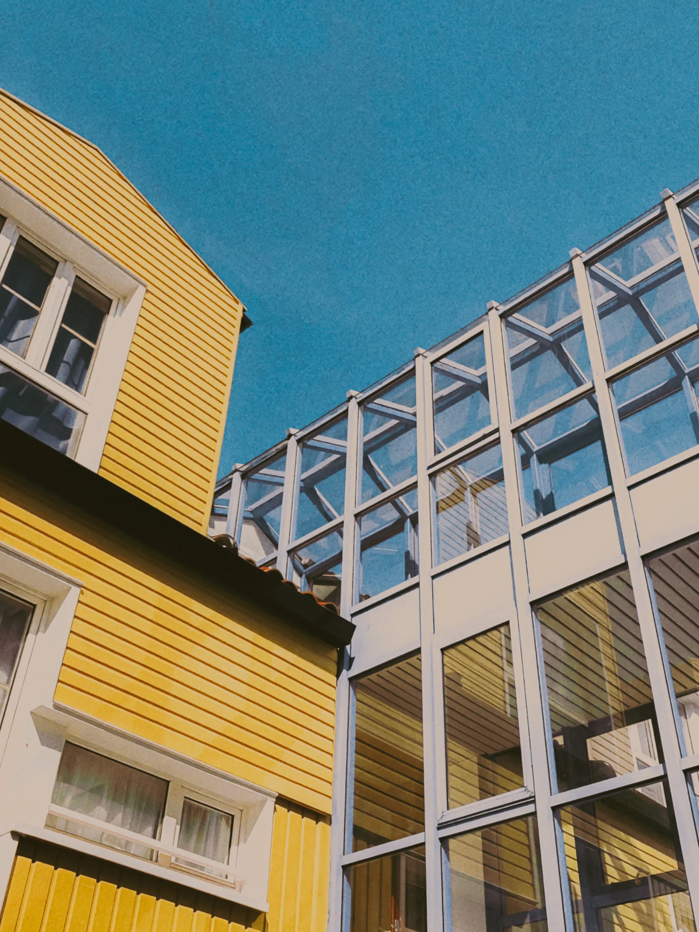 Facade de bâtiments modernes, l'un en bois jaune et l'autre en verre, sous un ciel bleu clair.