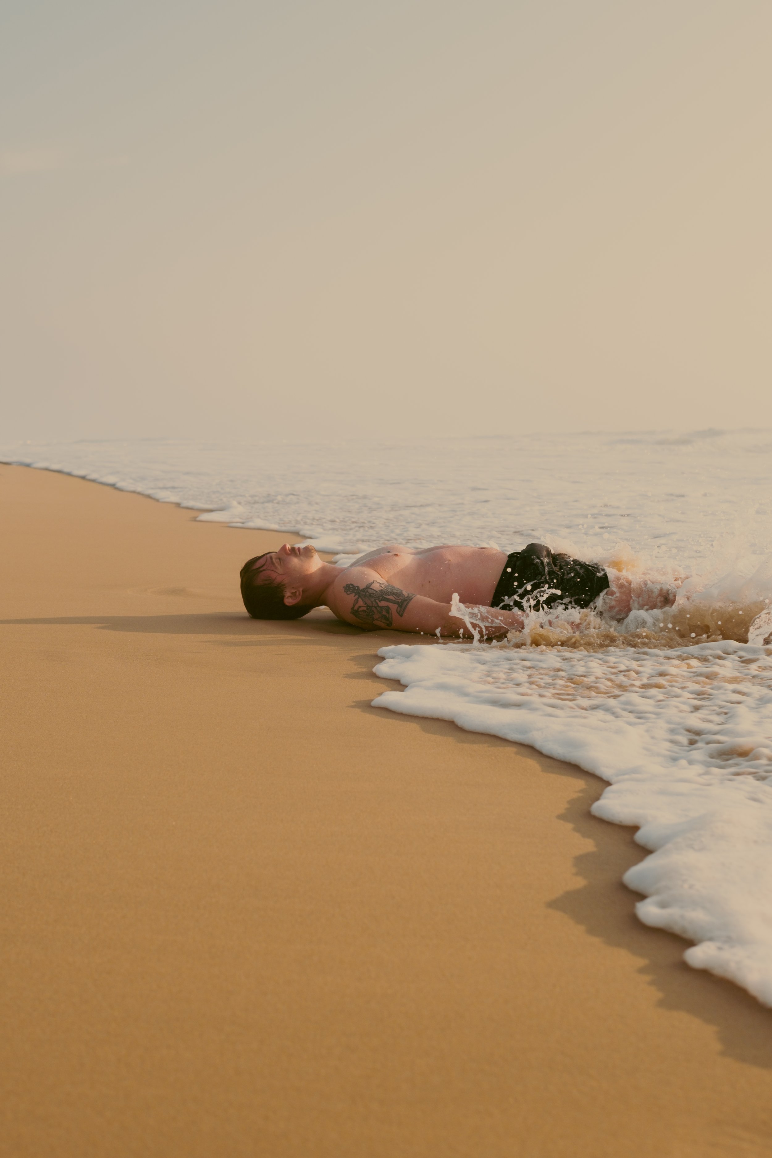 Un homme allongé sur la plage en bord de mer, en train de se détendre avec des vagues qui l'entourent.