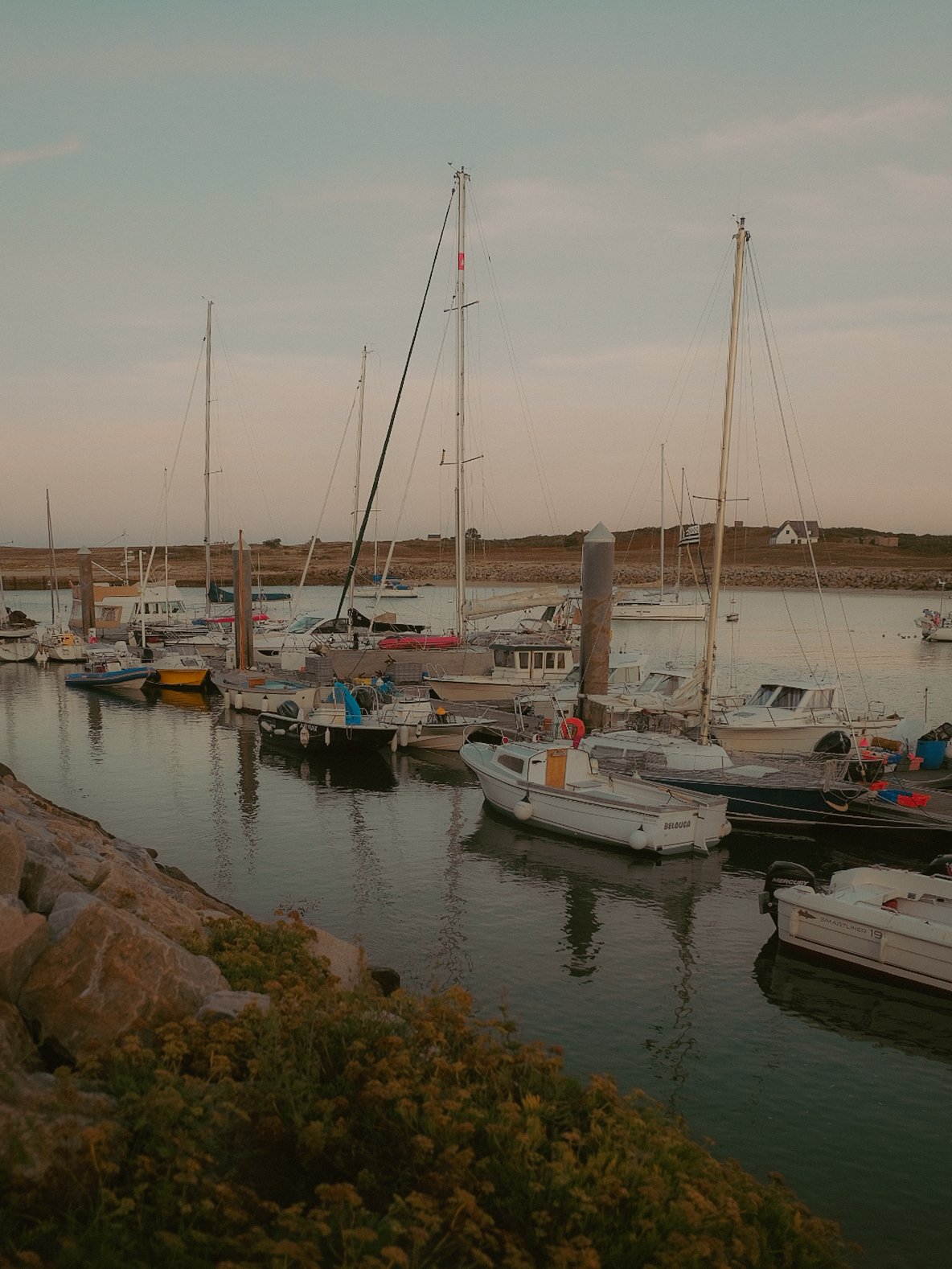 Un port de plaisance avec plusieurs bateaux amarrés, eaux calmes, ciel nuageux et terres en arrière-plan.