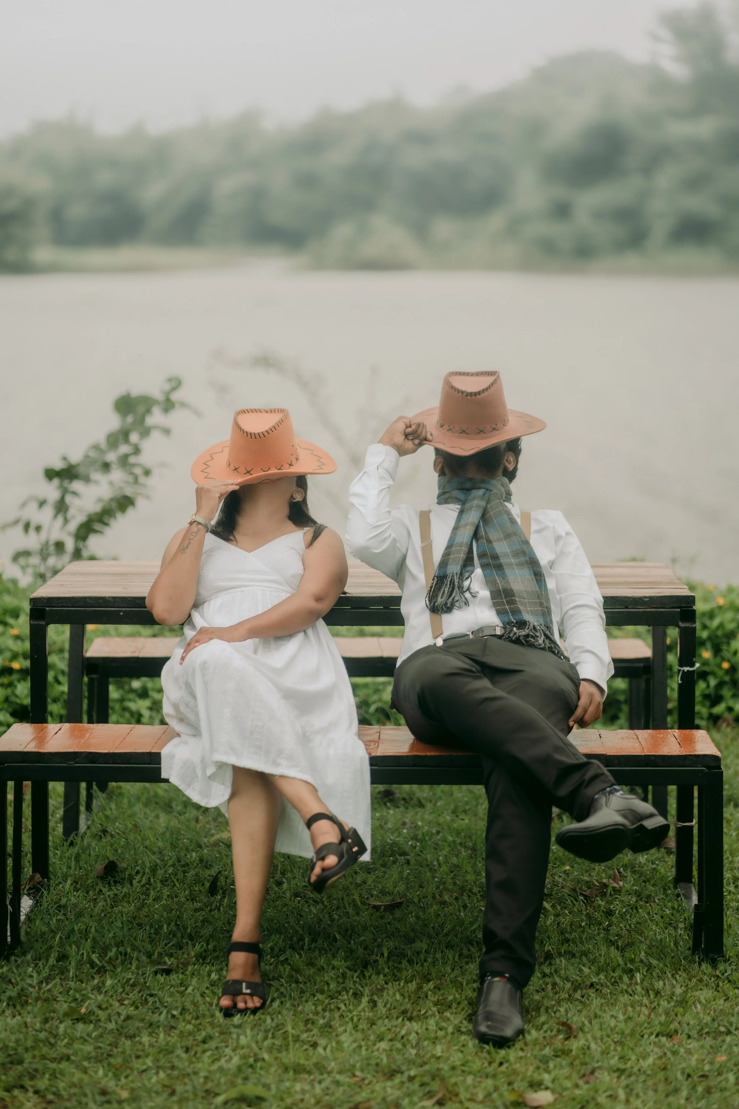 a couple in a relationship sitting on a bench in nature with hats on their faces - comfortable and secure with each other