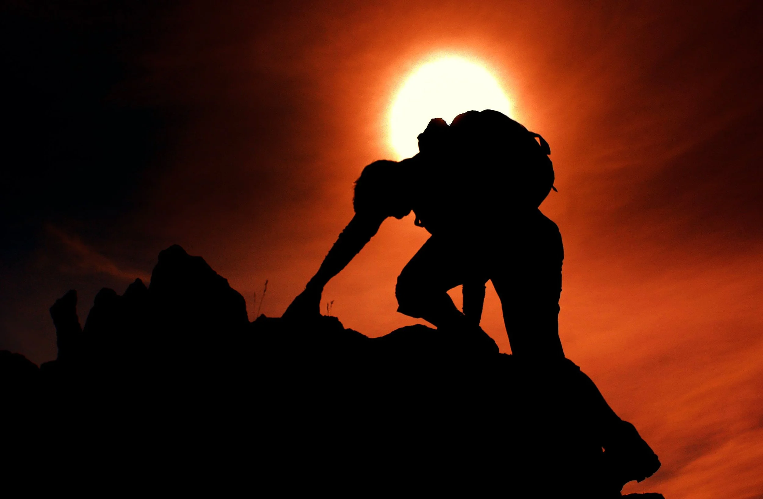 captivating photo of red sunset and silhouette of man climbing a mountain and rocks achieving his goals and mission