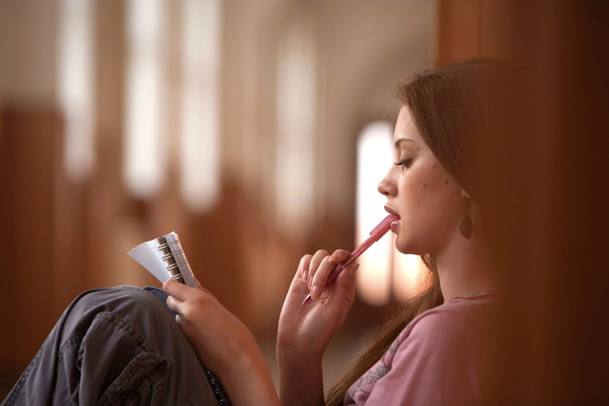 thoughtful and pensive woman sitting on the floor reading a notebook, with pen in mouth, considering therapy language and diagnoses