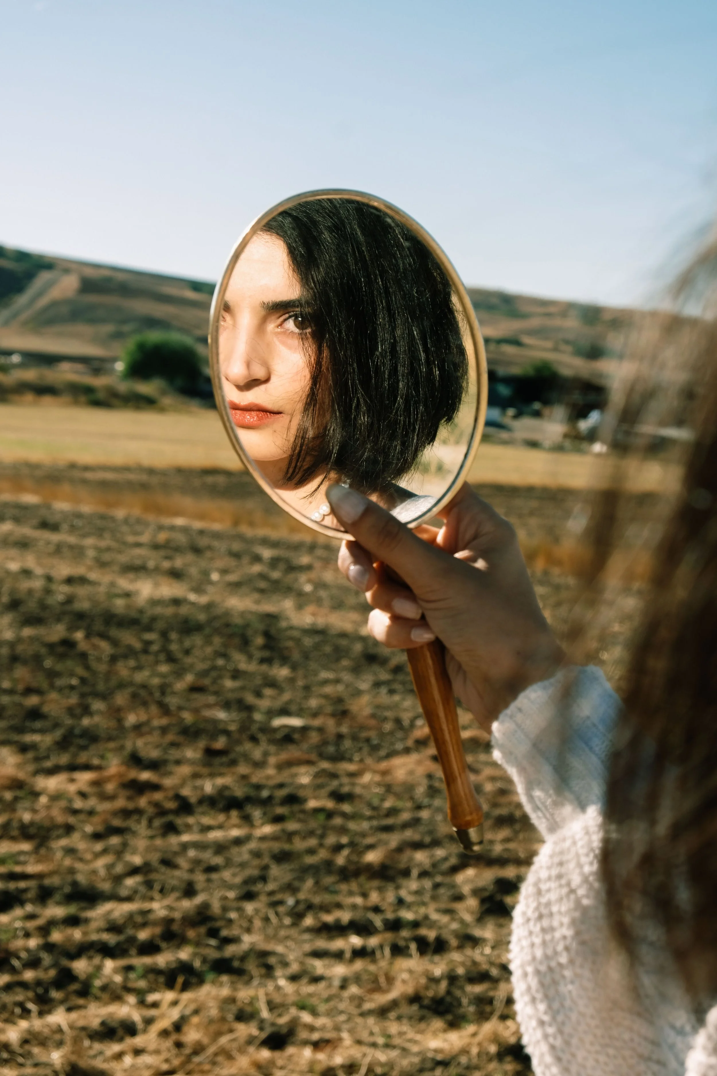 woman looking into mirror in nature judging herself and her decisions