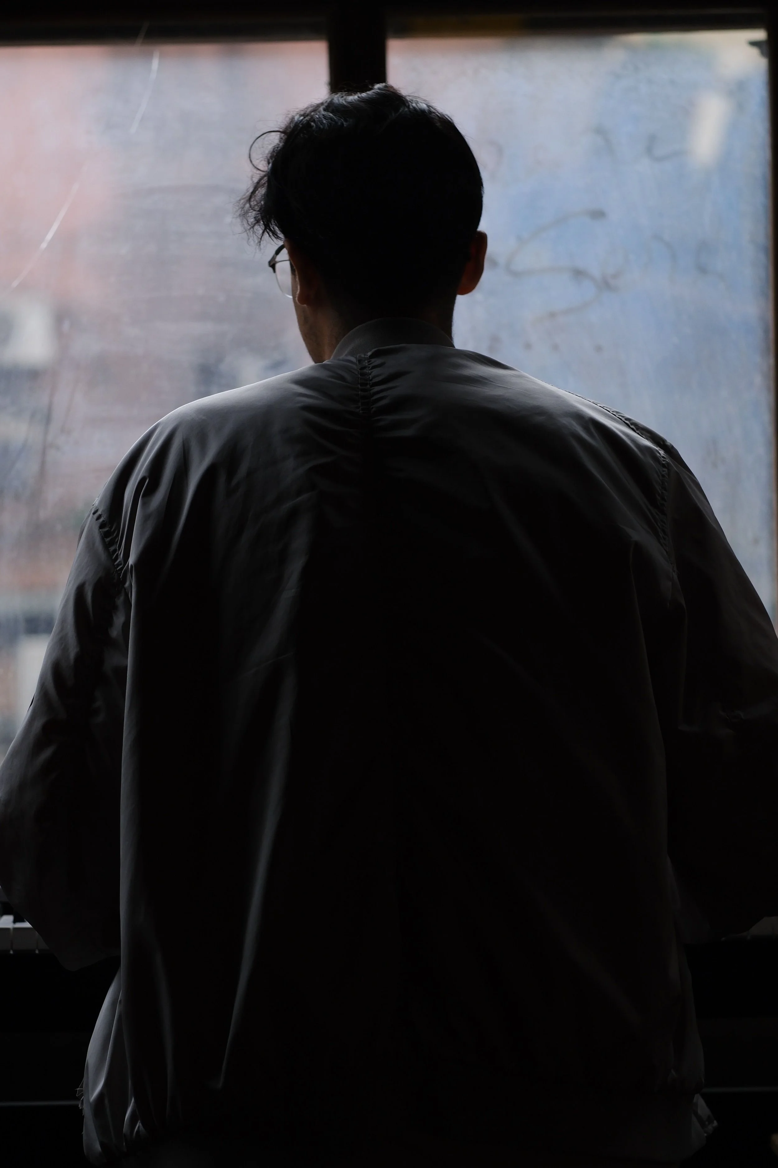 man looking out through dirty window feeling contemplative and pondering with a dark silhouette of his back showing