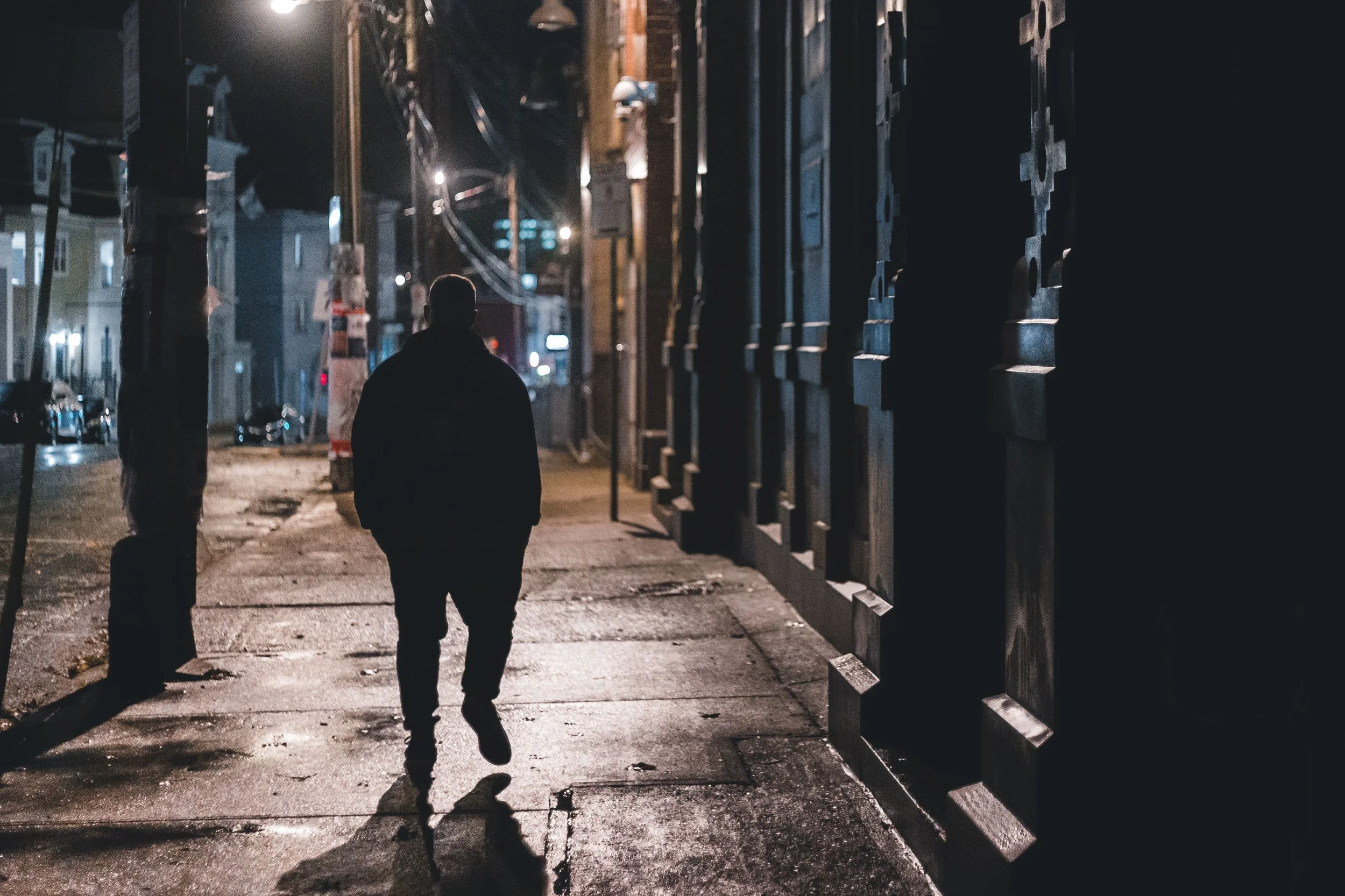 man walking alone on the street during the nighttime - dark city and shadows representing loneliness and mental health challenges