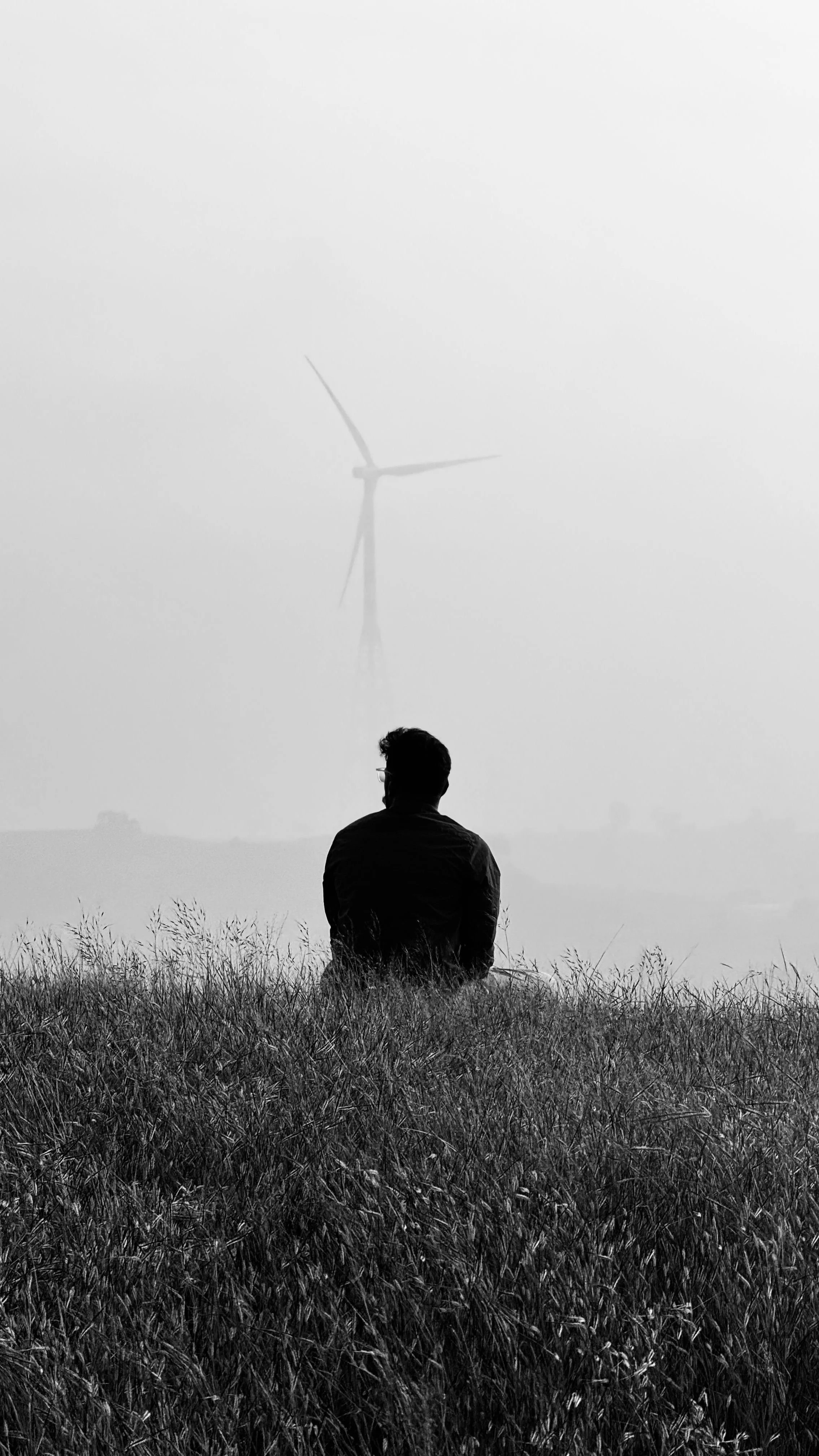 man sitting alone on a hill with grass with a windmill in the background