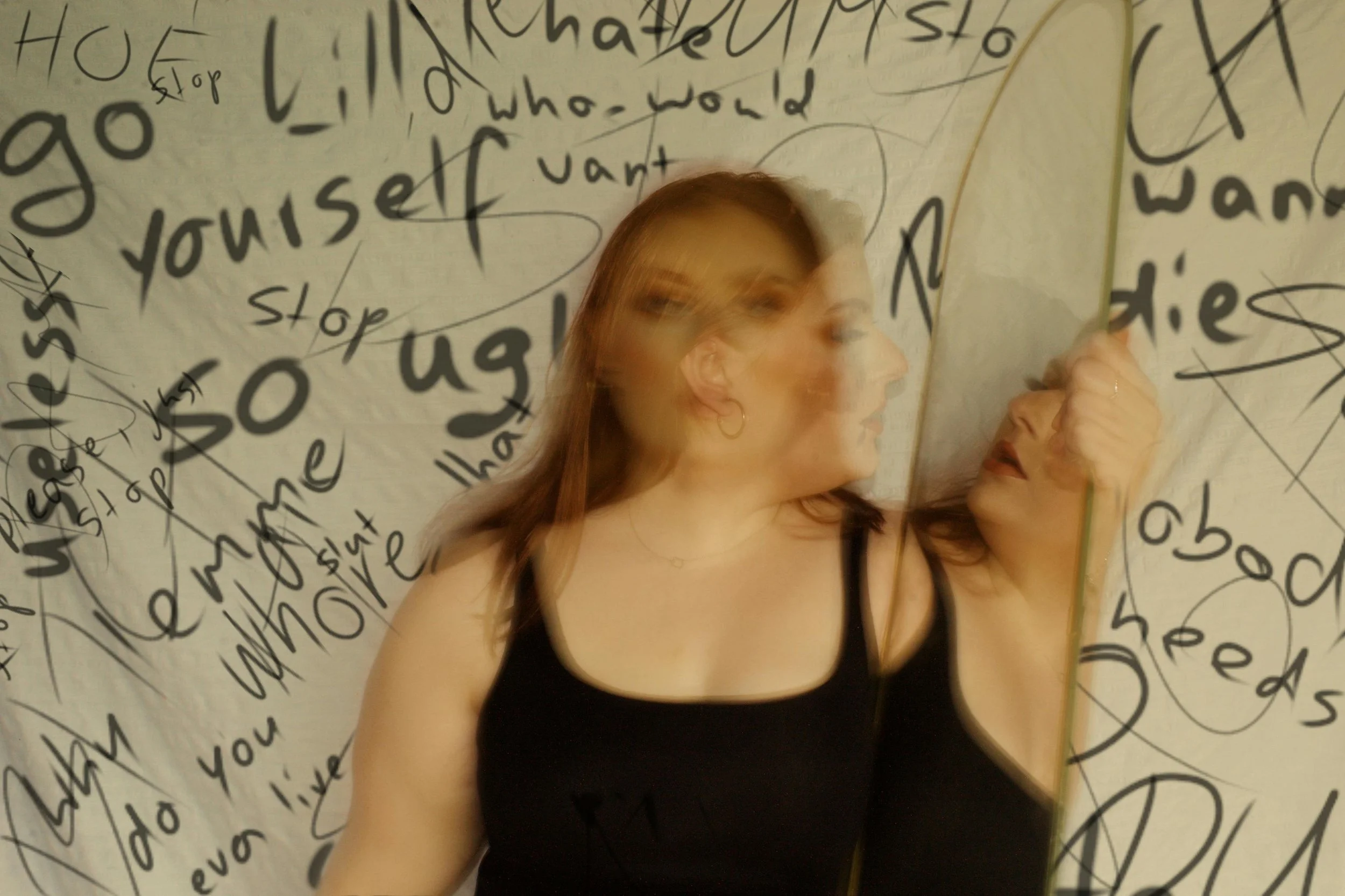 woman holding piece of mirror and the wall behind her has scribbles on it regarding self doubt and lack of confidence, low self esteem and self worth