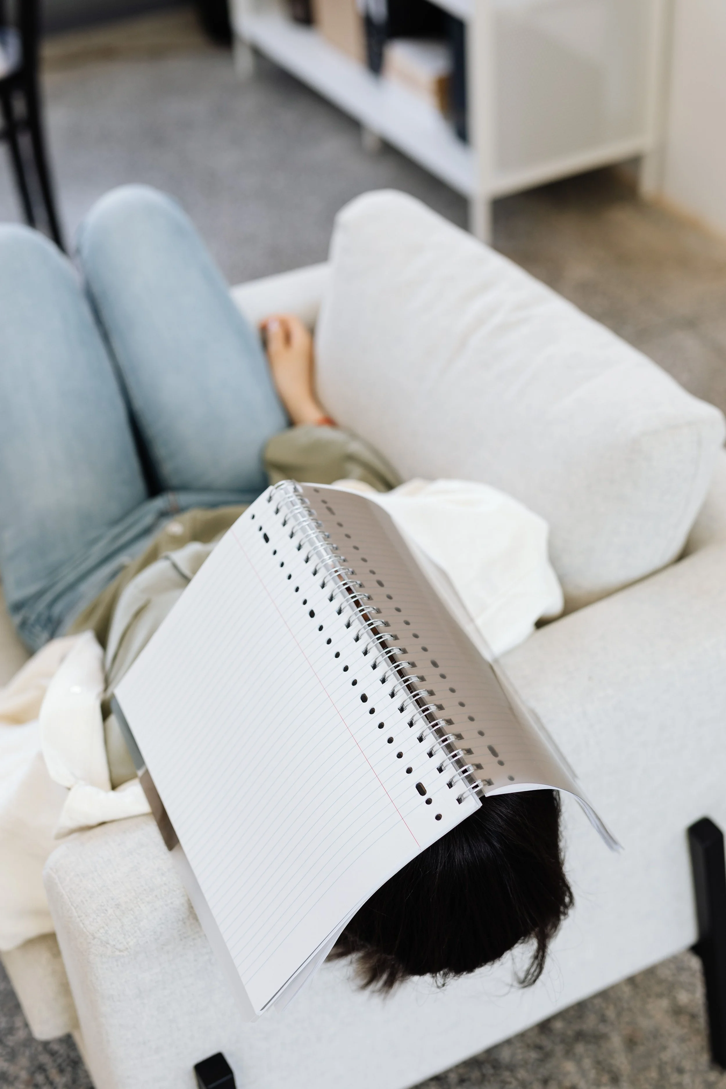 woman lying on coach with notebook on head giving up on answering all the questions and doing all the self care