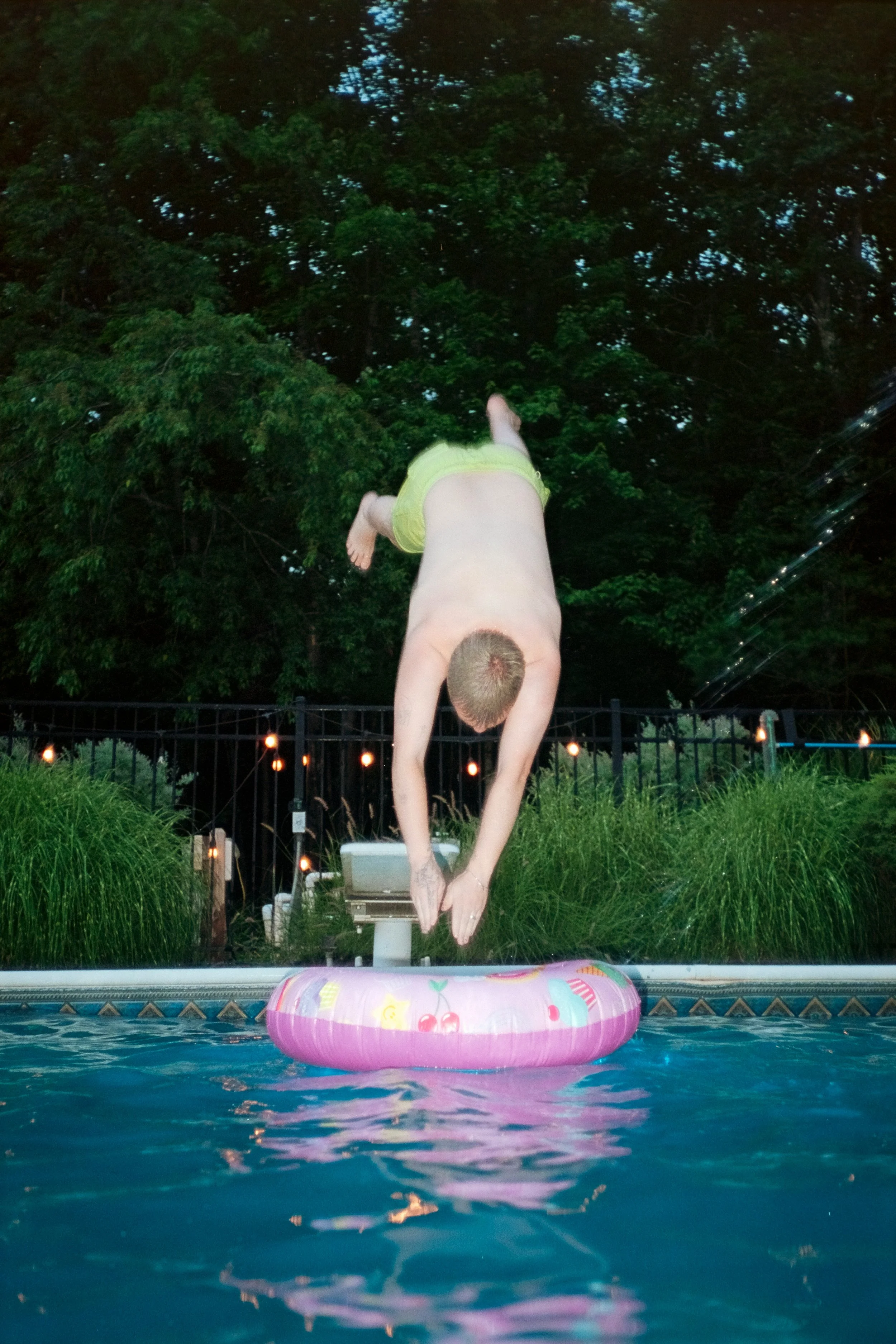 caucasian man diving into pool floaty with a background of green shrubs and nature
