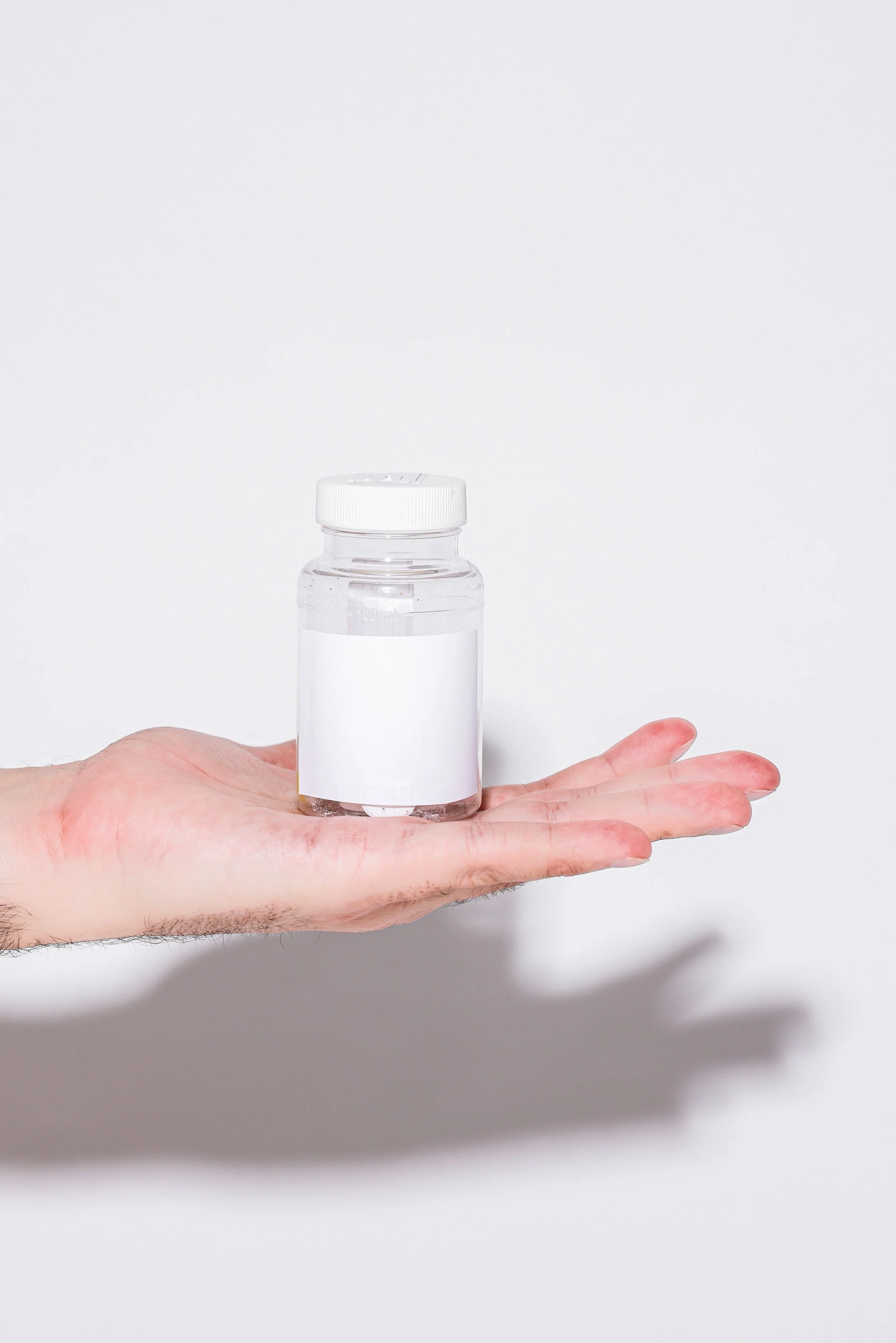 mans hand holding pill bottle with empty label on white backdrop - medication