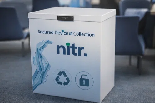 Large white collection box with Nitr branding, recycling and lock icons, labeled as a secured device of collection at an airport or public space.