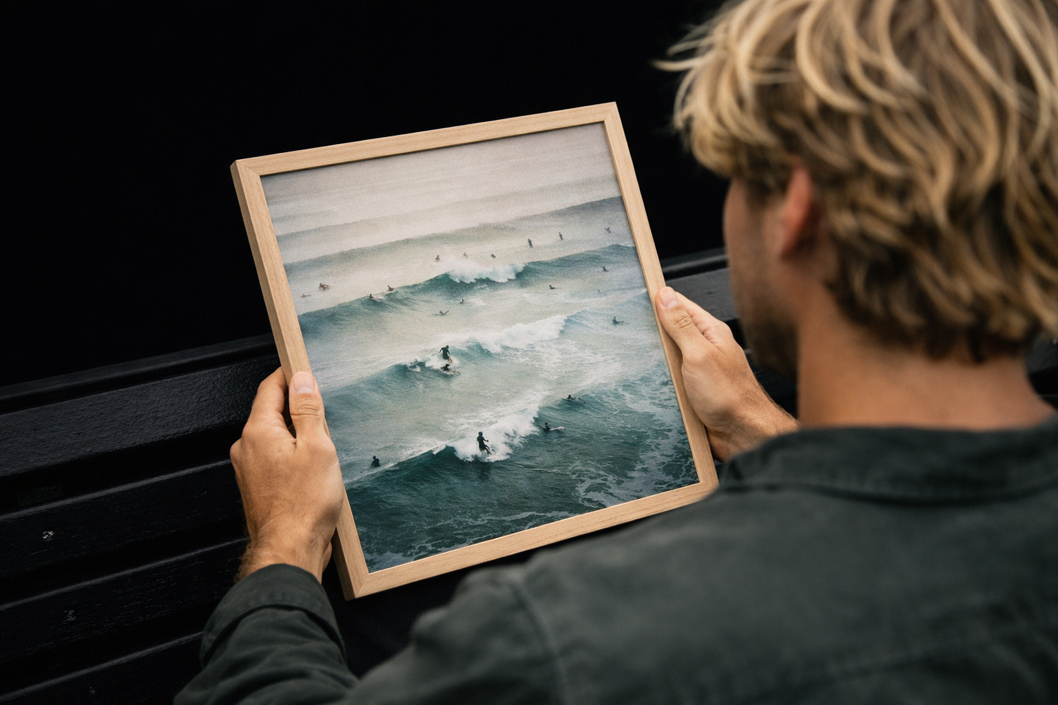 A person holding a framed picture of a surfing scene with waves and surfers in the ocean.