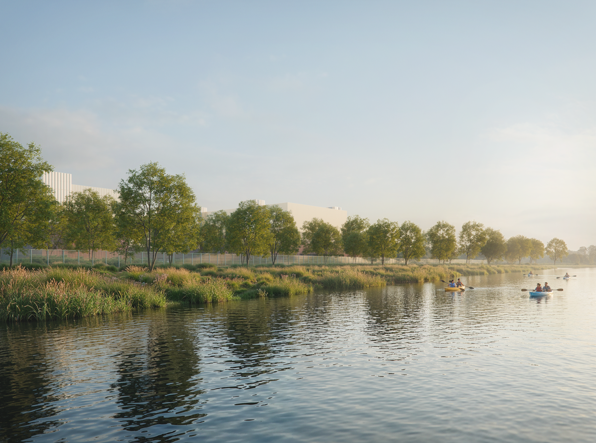 People kayaking on a calm river with green trees and grasses along the bank, and modern white buildings in the background, under a partly cloudy sky.