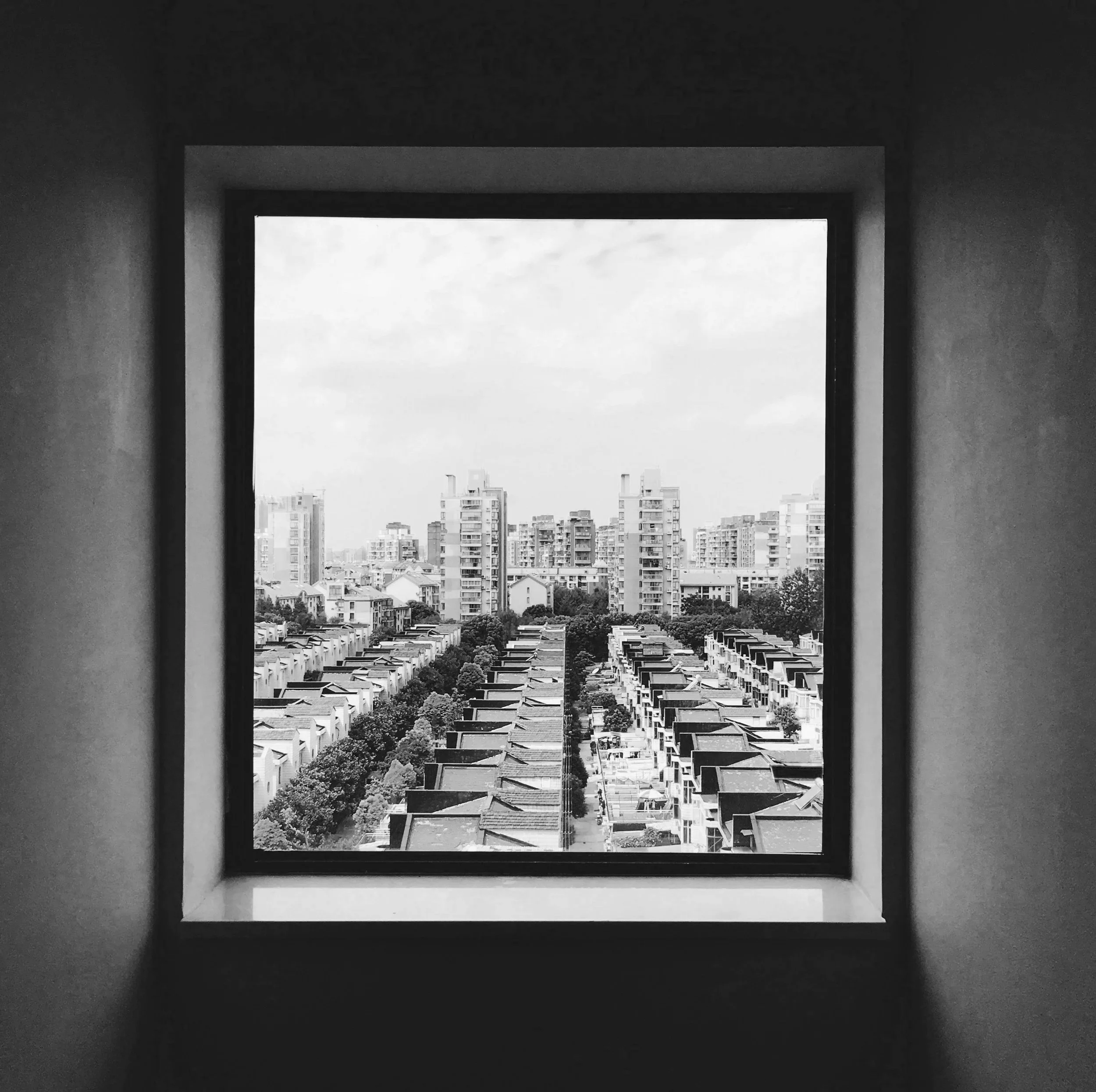 Black and white photo of cityscape seen through a window, showing residential buildings and apartment complexes.