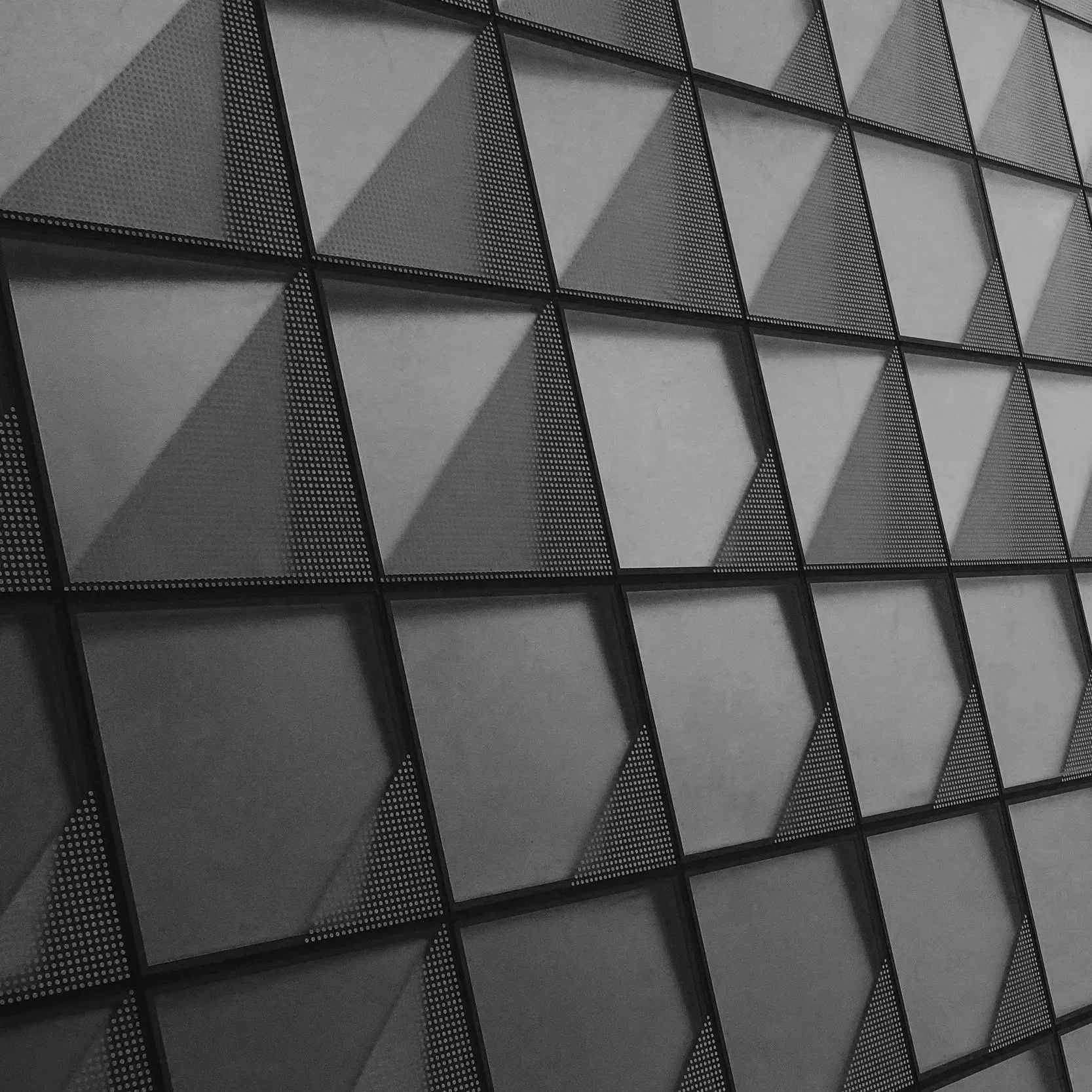 Close-up of a modern building's exterior with geometric pattern of square and triangular panels, some with dotted textures, creating a repeating angular design.