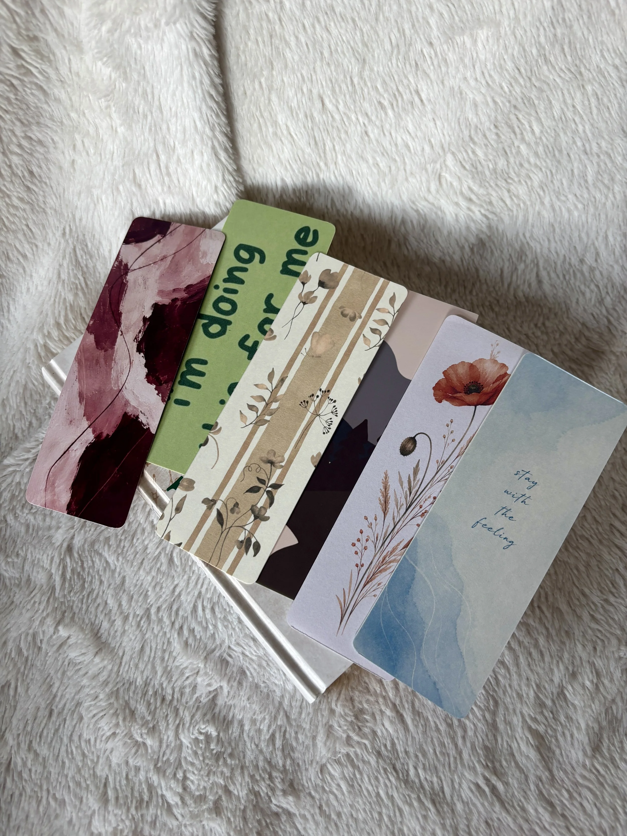 Close-up of handmade bookmark designs featuring a red poppy, burgundy abstract painting and beige botanical pattern.