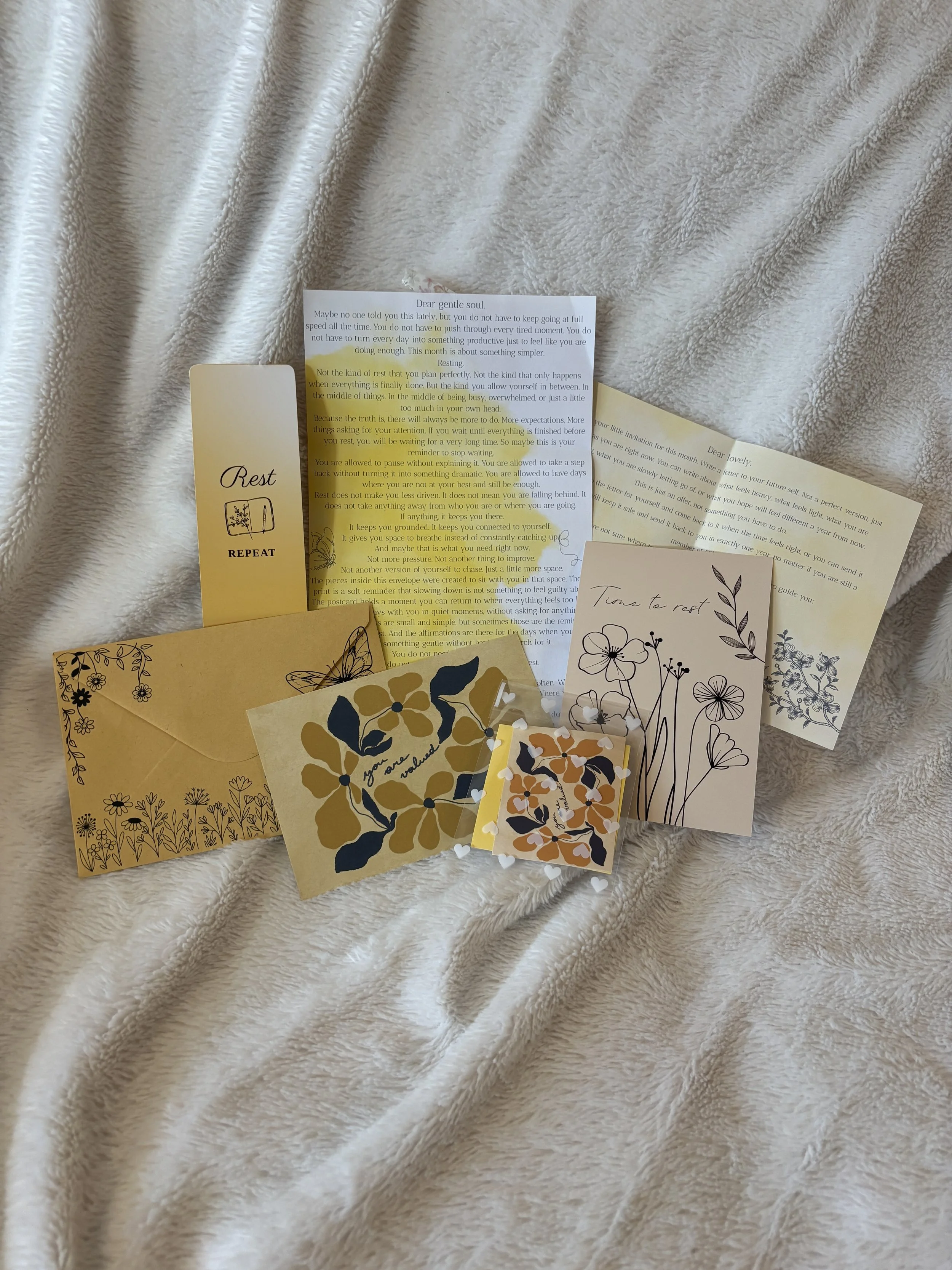 Collection of greeting cards and envelopes with floral and botanical designs, placed on a soft, cream-colored textured fabric background.