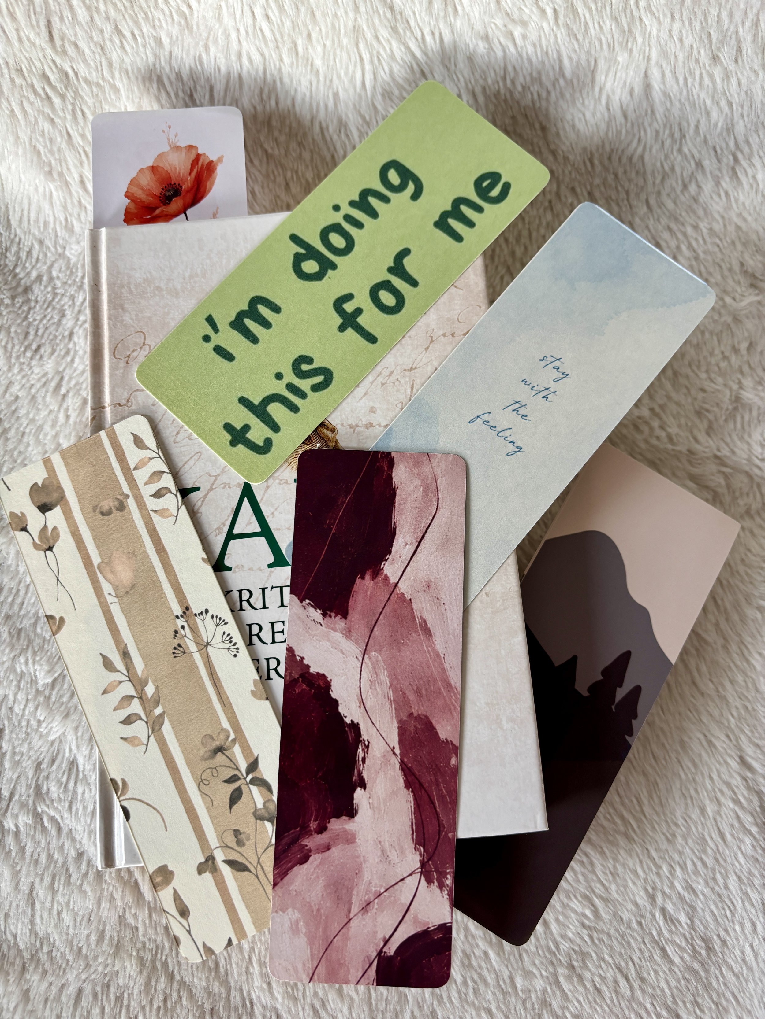 Six unique The Femme Letter bookmarks in floral, abstract and typographic designs arranged on a book.
