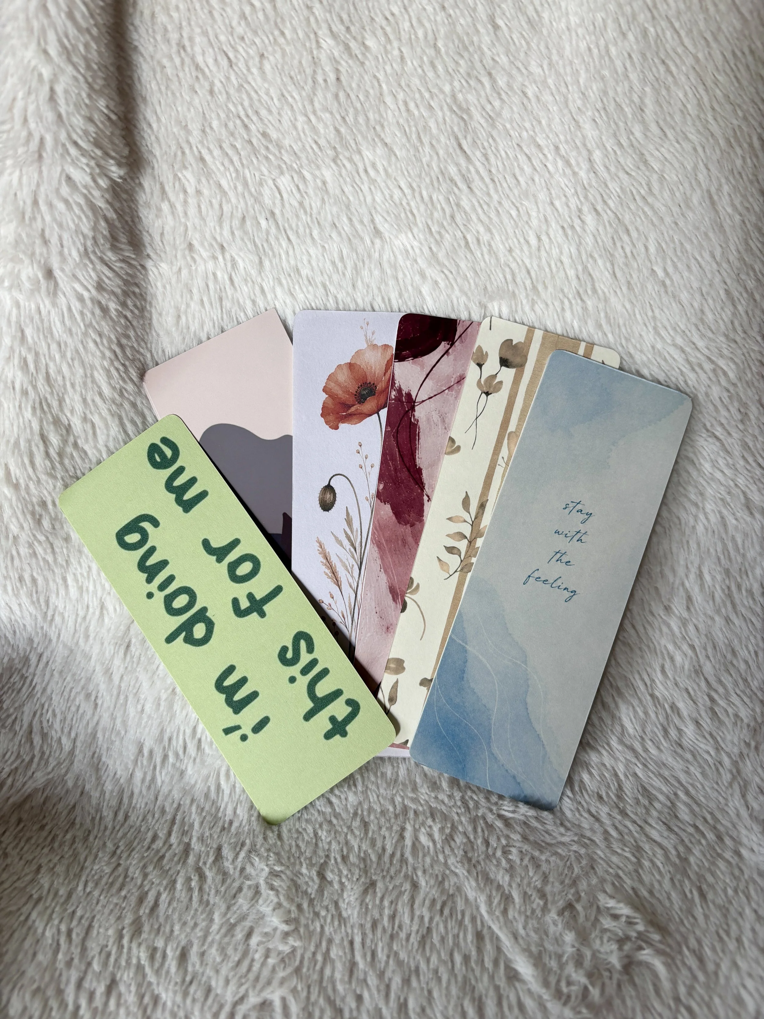 Close-up of handmade bookmark designs featuring a red poppy, burgundy abstract painting and beige botanical pattern.