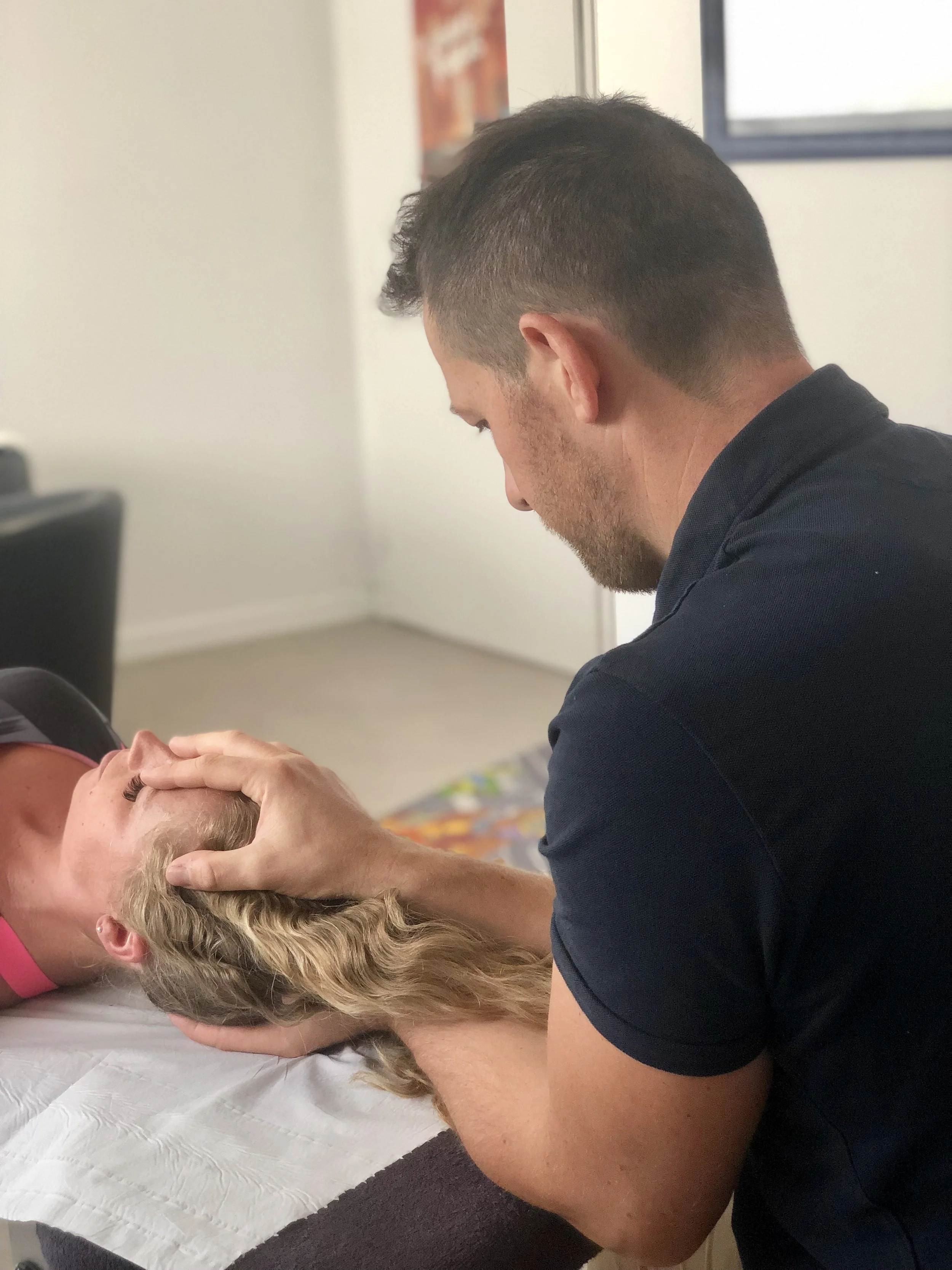 Un homme pratique un soin sur une femme allongée, en position de relaxation, dans une pièce lumineuse.