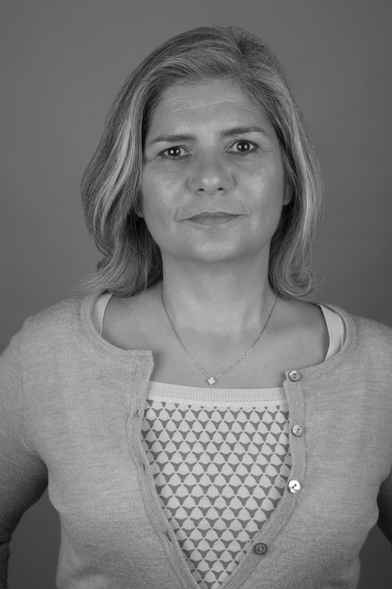 Black and white portrait of a woman with shoulder-length hair, wearing a cardigan over a patterned top, and a necklace.