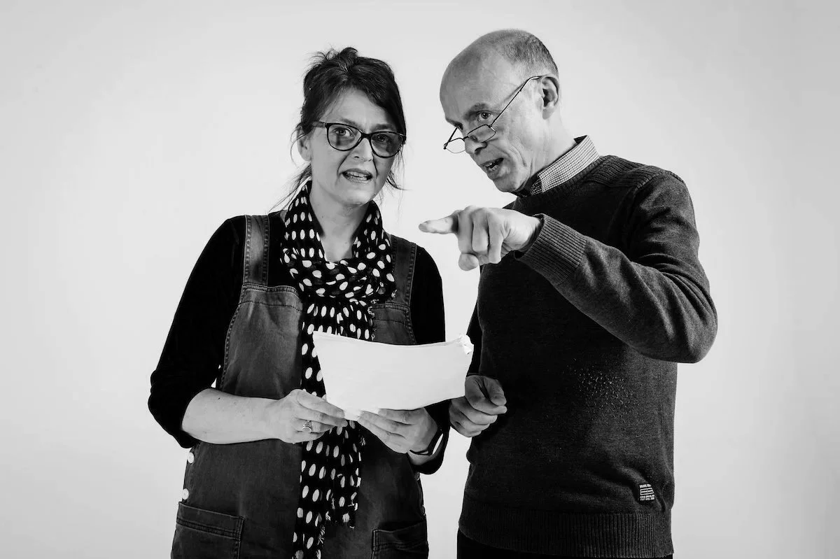 A man and woman looking at a document, with the man pointing at it, both with serious expressions.