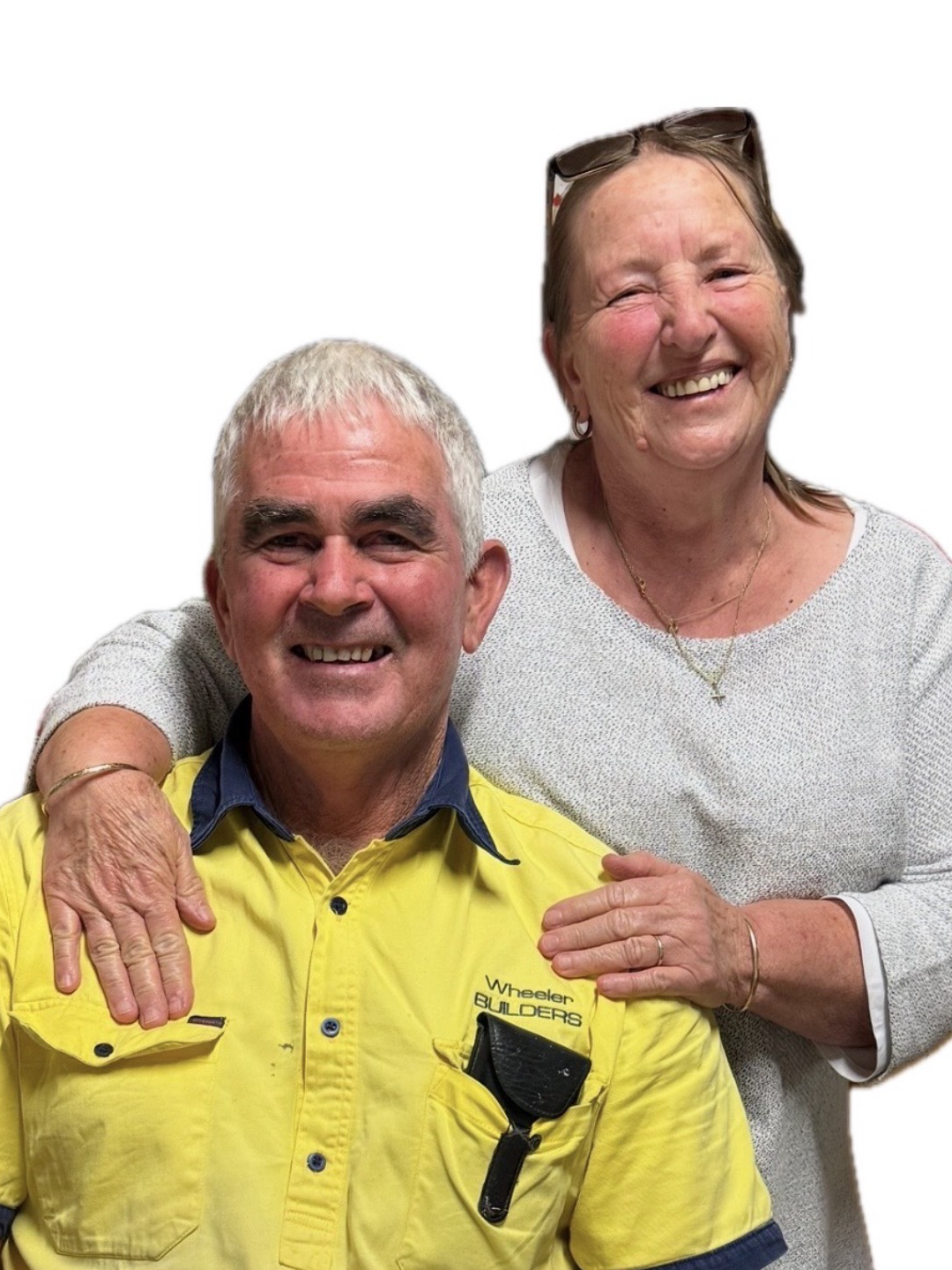 Smiling elderly man in yellow jacket sitting with arm around smiling elderly woman in white sweater, with hands on his shoulders, against plain white background.