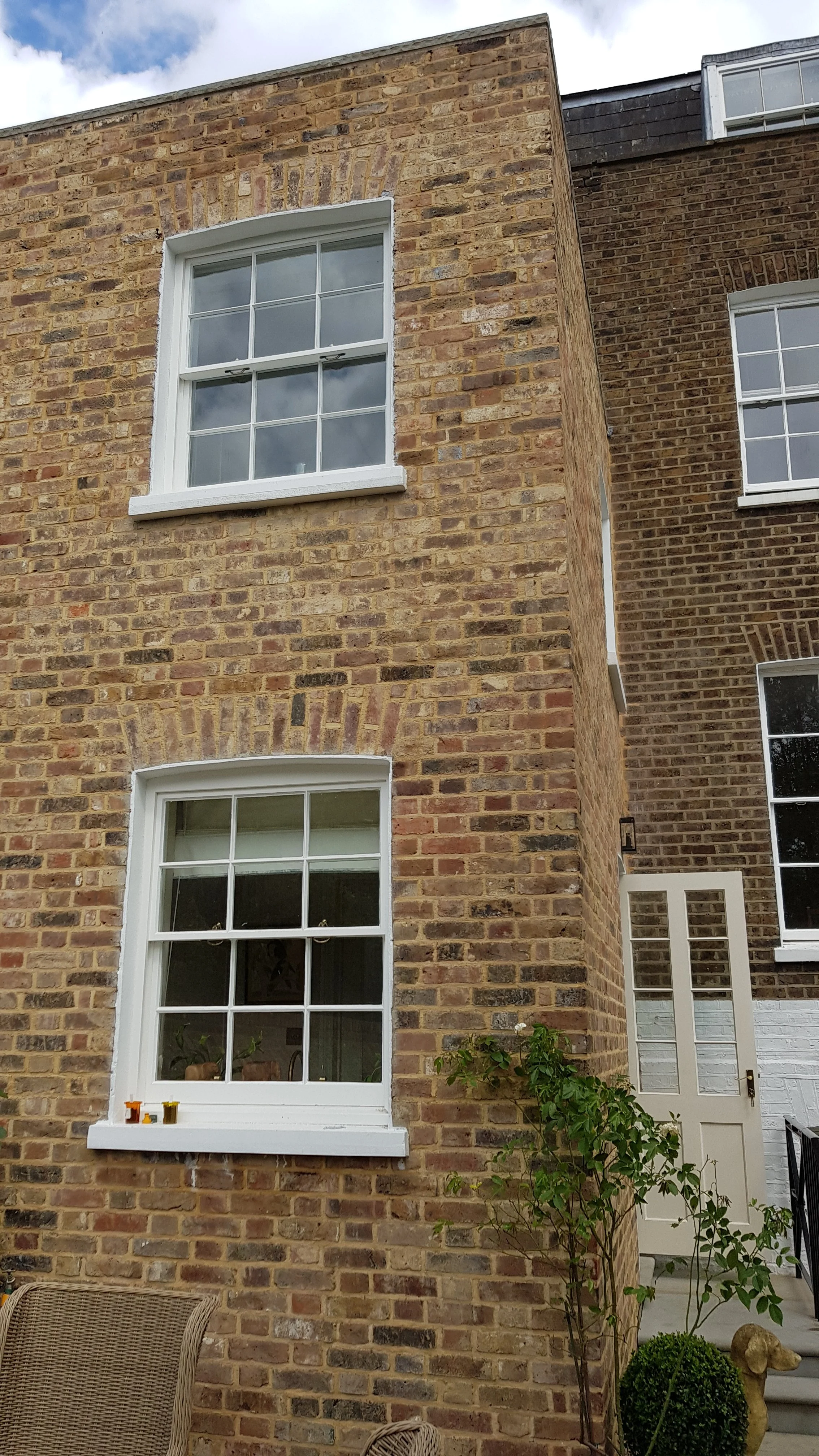 Close-up of a brick house with a new extension for more living space. The new extension has two white-framed windows, one above the other, and a white door.