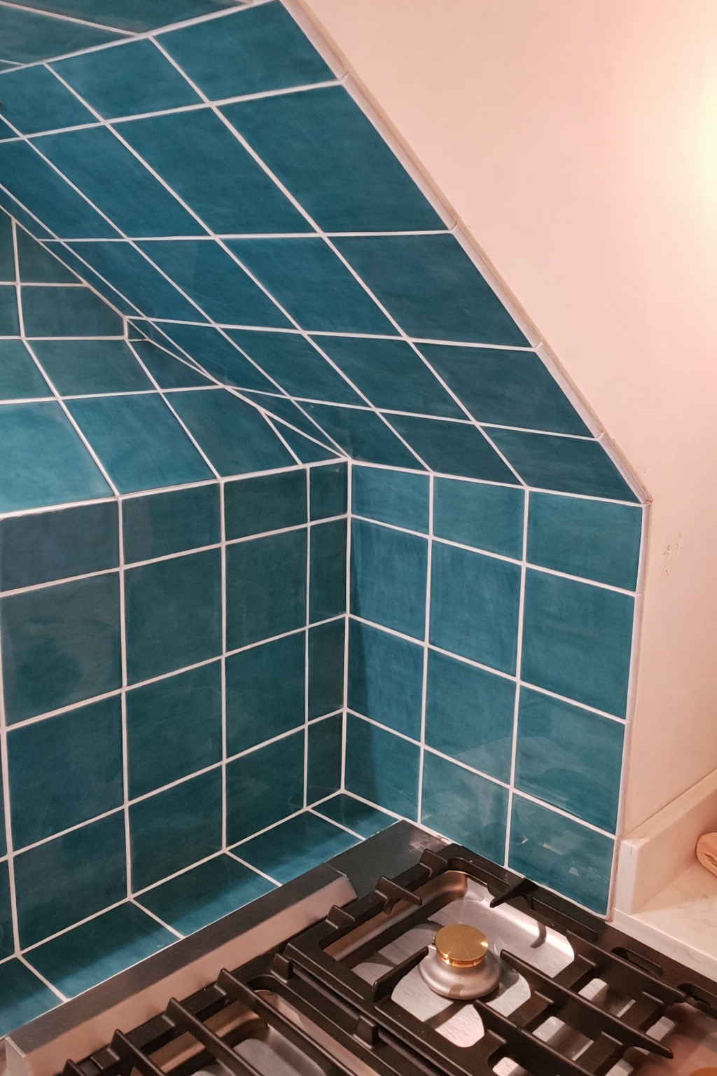 A close-up of a kitchen stove with new teal tiles as the backsplash, featuring a curved design and white grout.