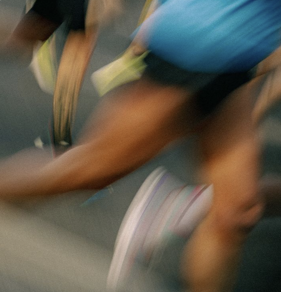 Blurred image of a person in athletic clothes riding a skateboard on a gray surface.