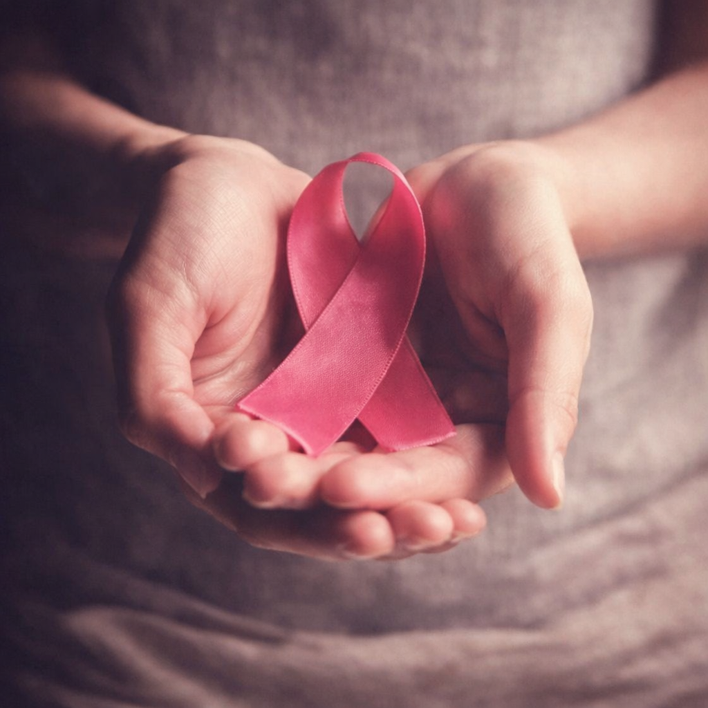 A person holding a pink awareness ribbon in their hands.