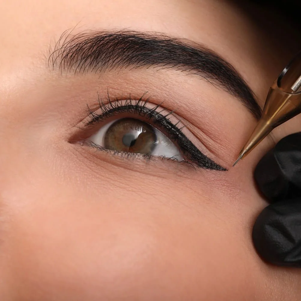 A close-up of a woman's eye being makeup-lined with a black eyeliner pencil.