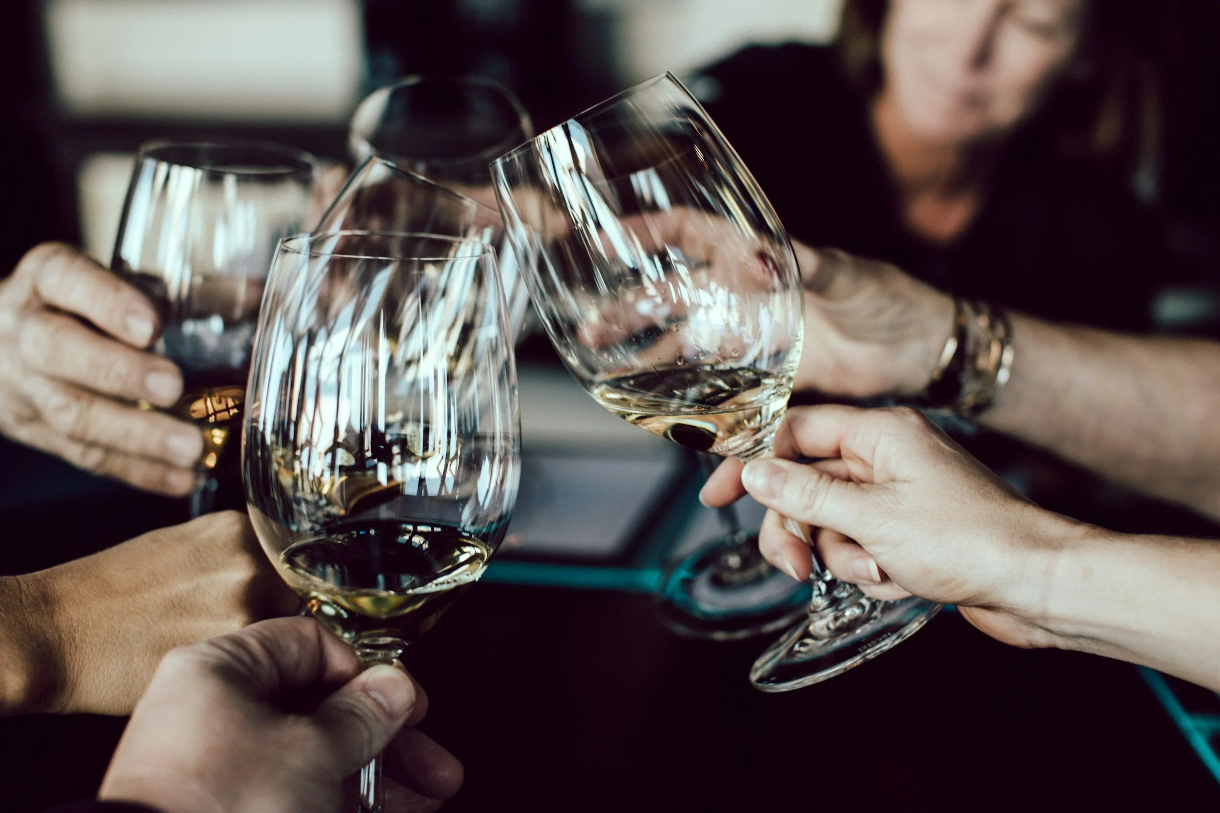 Four people clinking glasses of white wine during a celebration or gathering.