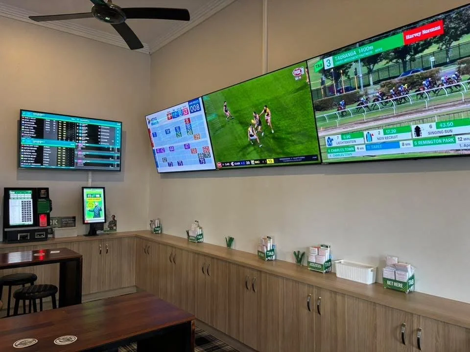 Sports betting lounge with multiple screens showing horse racing and sports events, betting kiosks, and tables.