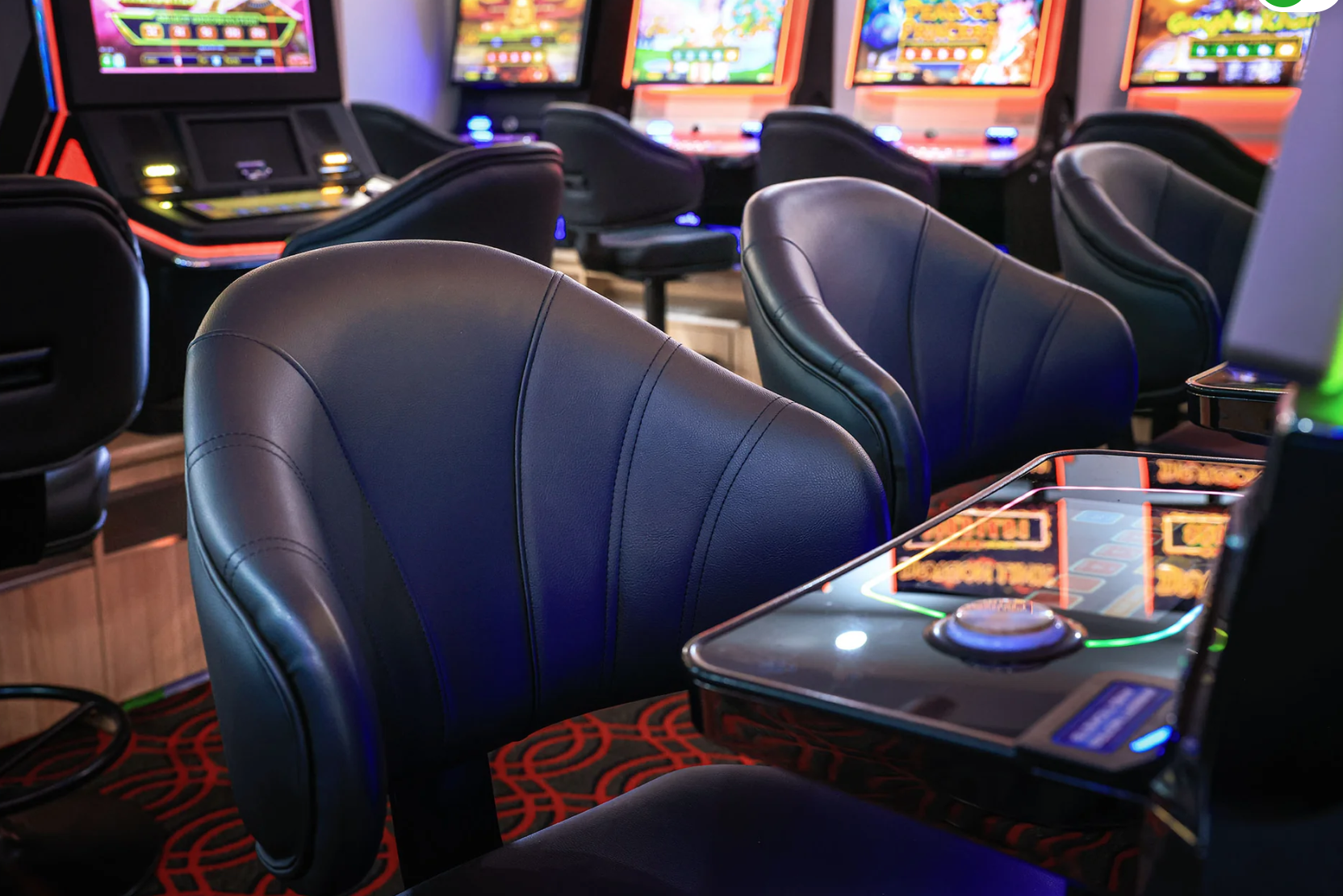 Empty black leather chairs and slot machines inside a casino.