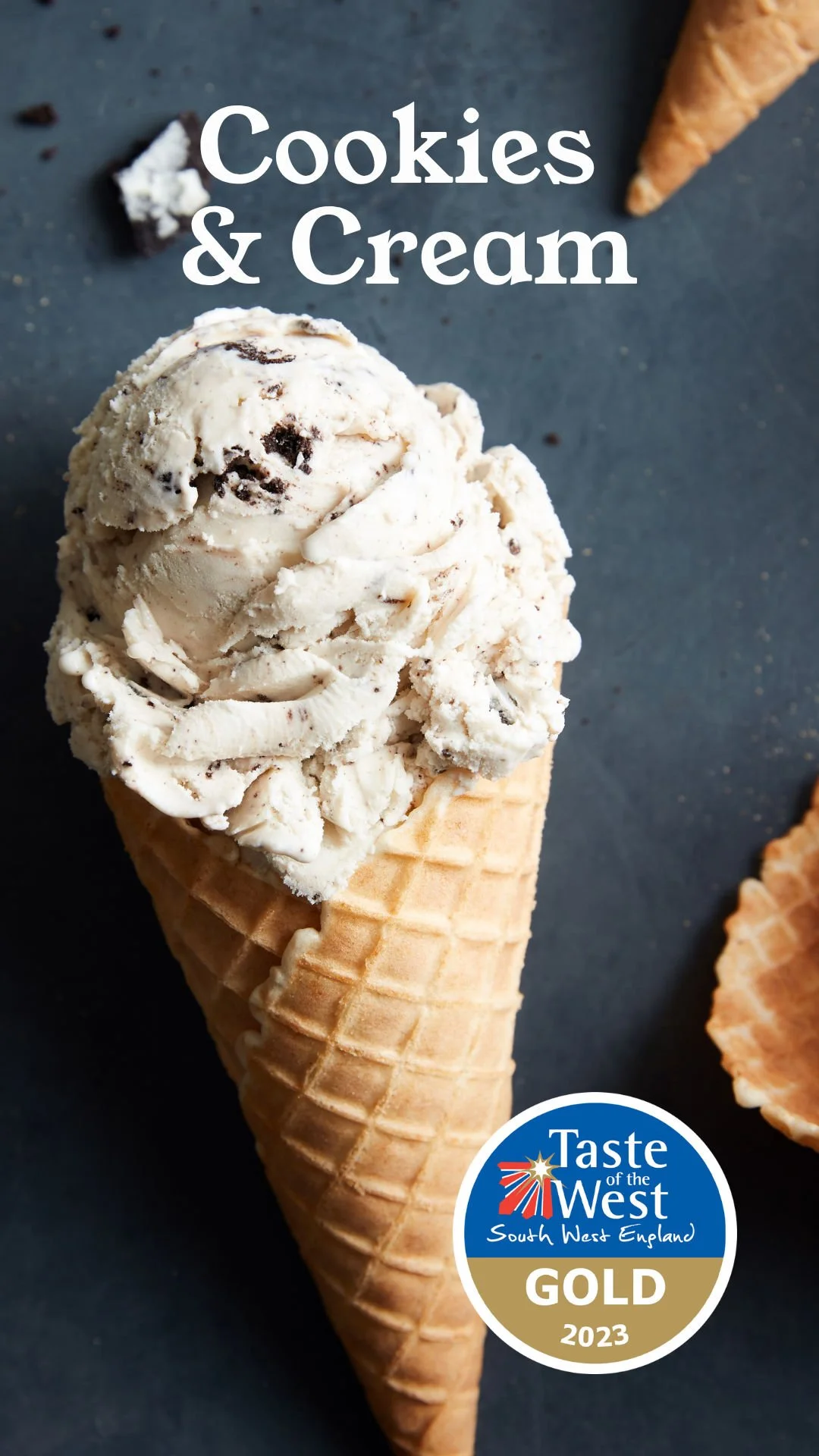 A cone of cookies and cream ice cream with bits of chocolate in a waffle cone, on a dark background, with the text "Cookies & Cream" and a gold medal sticker from Taste of the West South West England 2023.
