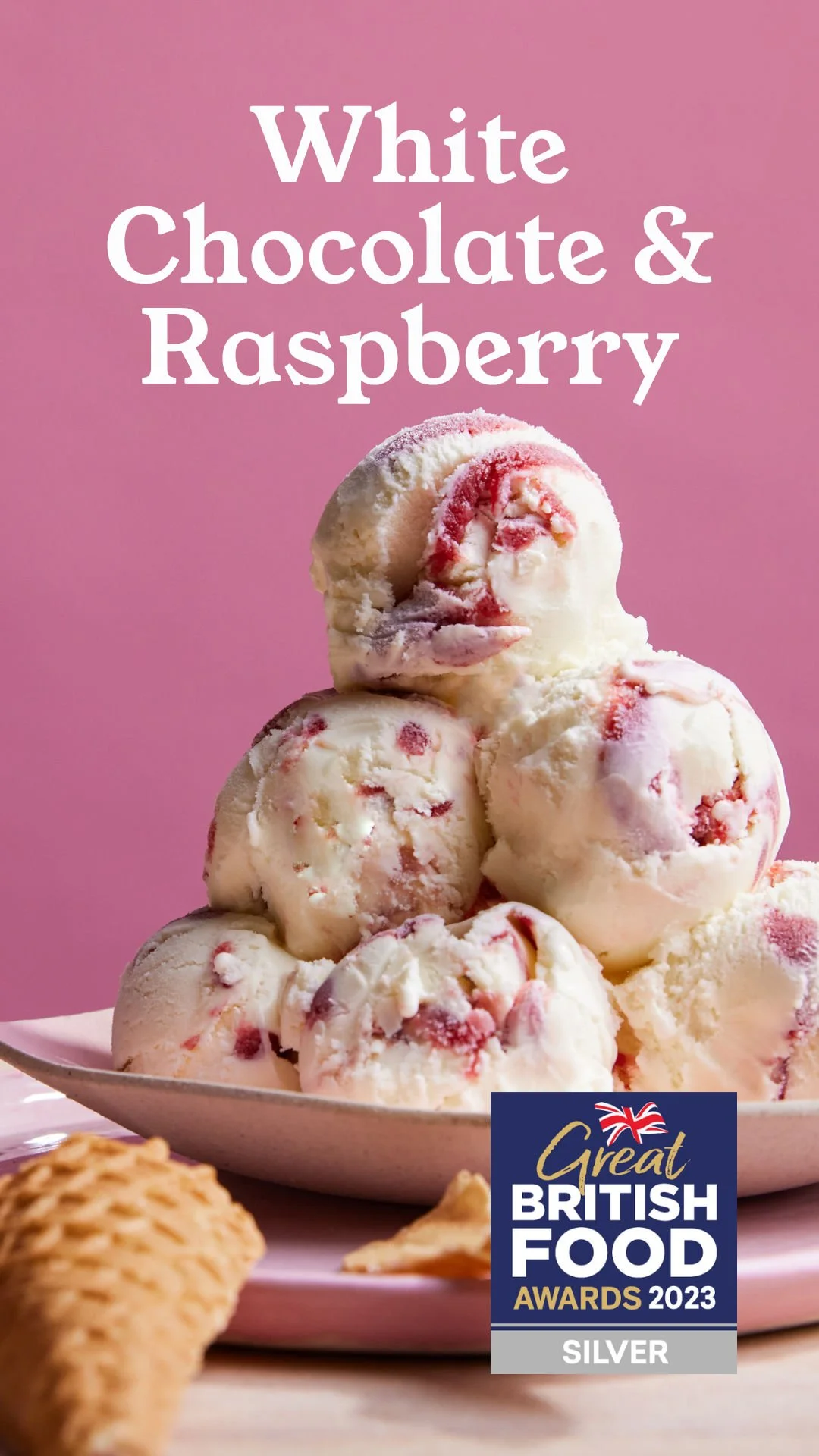 A bowl of white chocolate and raspberry ice cream balls on a pink background, with a biscuit in the foreground and a 'Great British Food Awards 2023 Silver' badge in the corner.