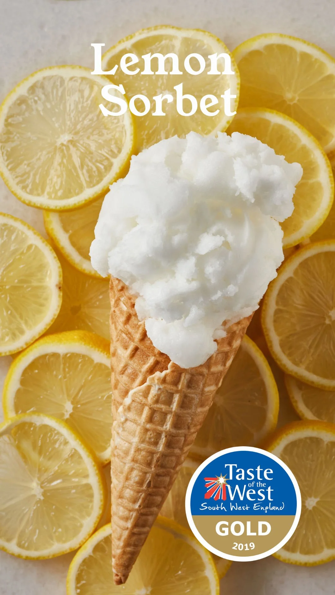 Lemon sorbet ice cream in a waffle cone with sliced lemons in the background and a 'Taste of the West South West England Gold 2019' award sticker.