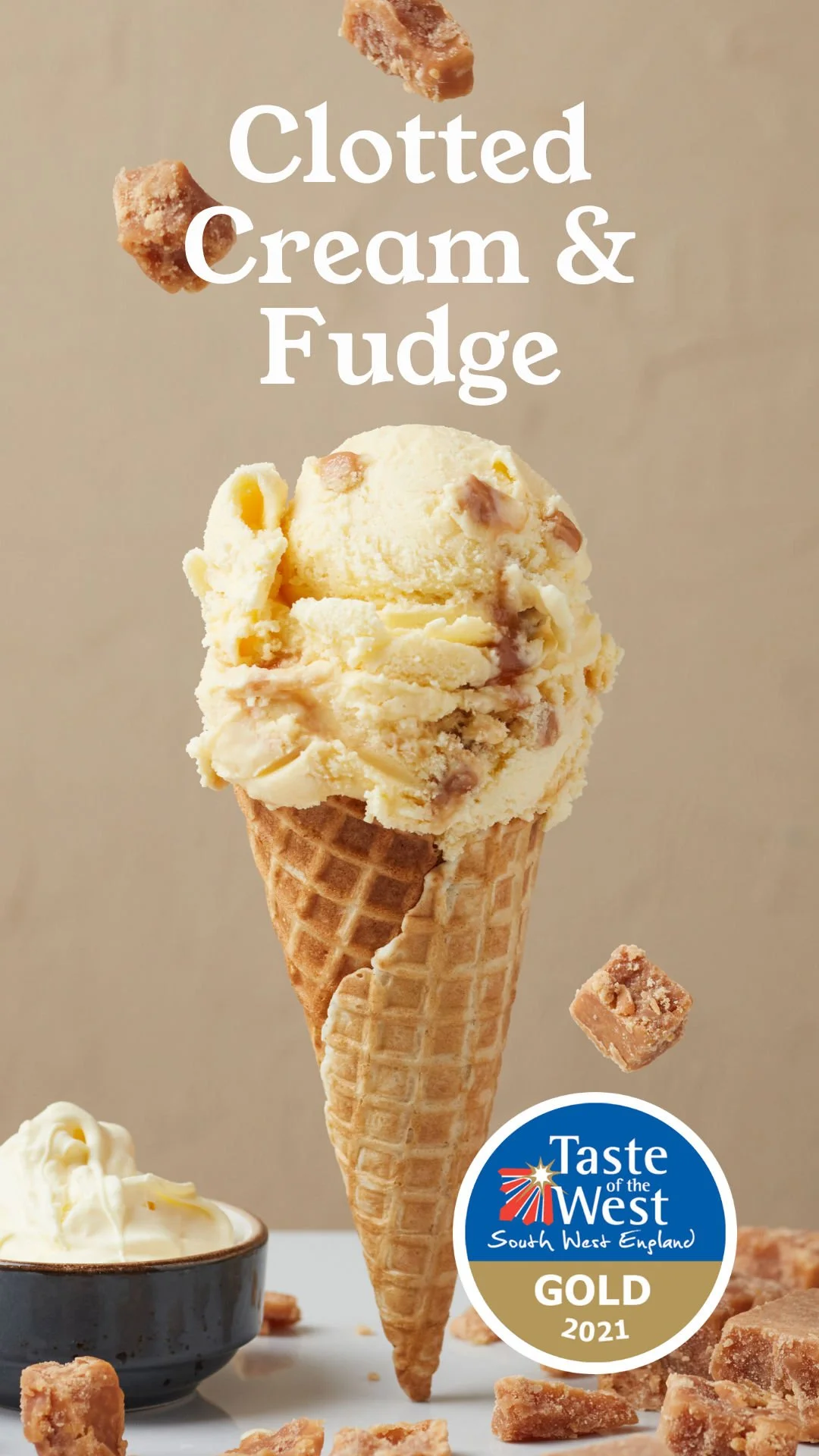 A cone filled with ice cream topped with fudge pieces, with pieces of fudge and a small bowl of cream nearby, and a label indicating it won a 2021 Taste of the West South West England Gold award.