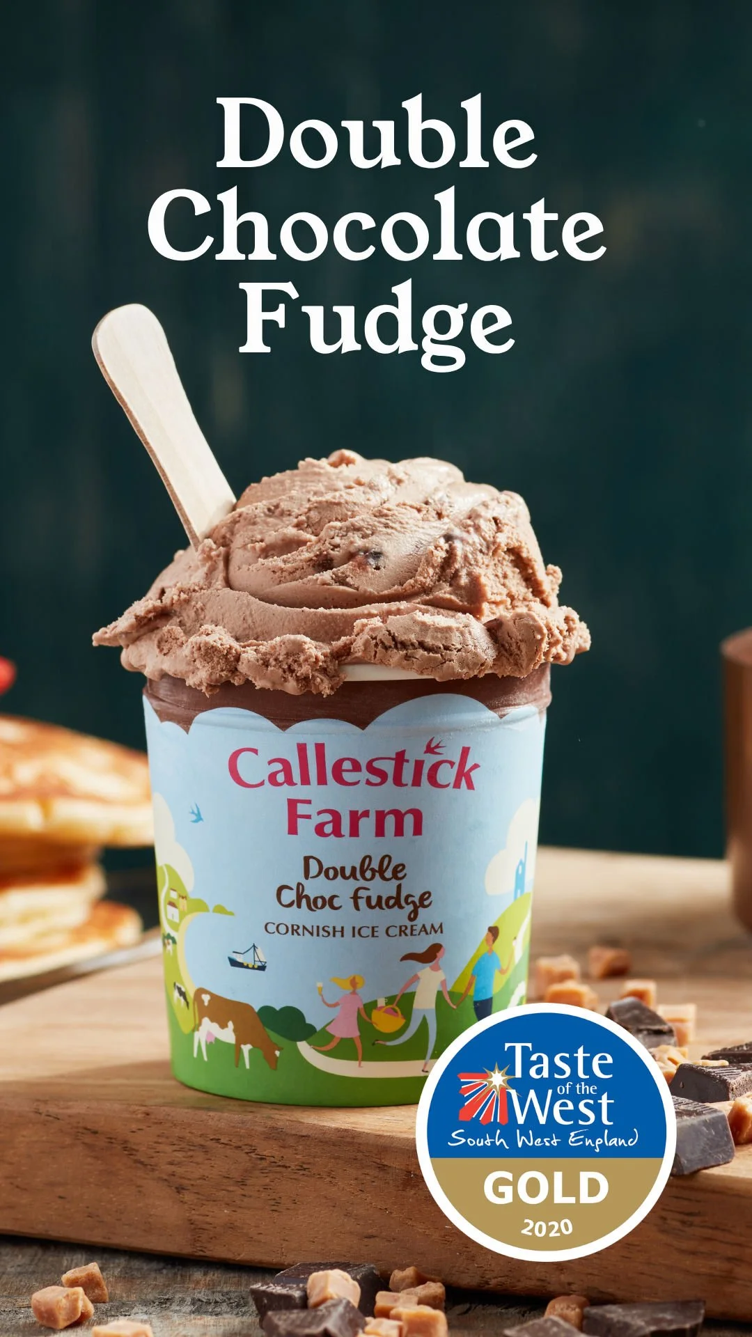A cup of Callestick Farm double chocolate fudge ice cream with a wooden spoon, placed on a wooden surface with chocolate chunks around, featuring a Taste of the West South West England Gold award logo from 2020.