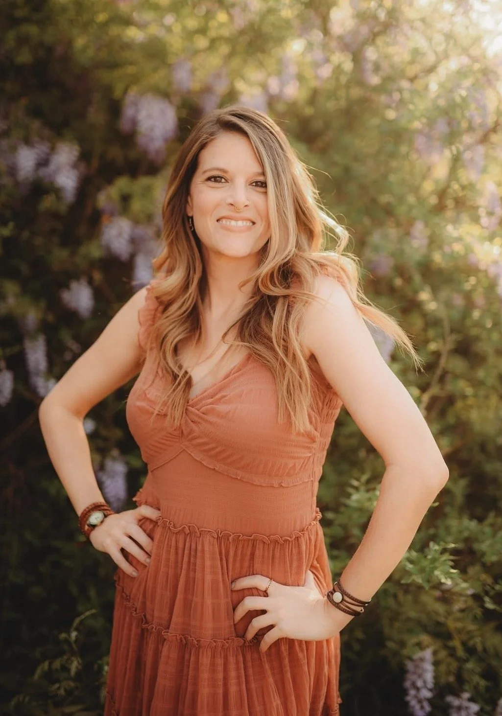A woman with short blonde hair sitting on a beige bench, writing in a notebook, with a large green plant and framed abstract art in a room with sunlight and shadows.