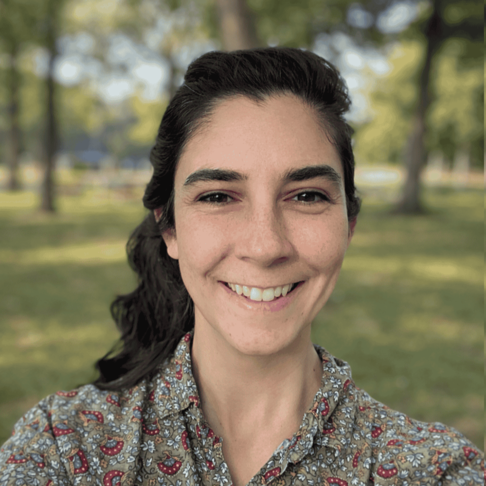 Close-up of a woman smiling in a park with trees and grass in the background.
