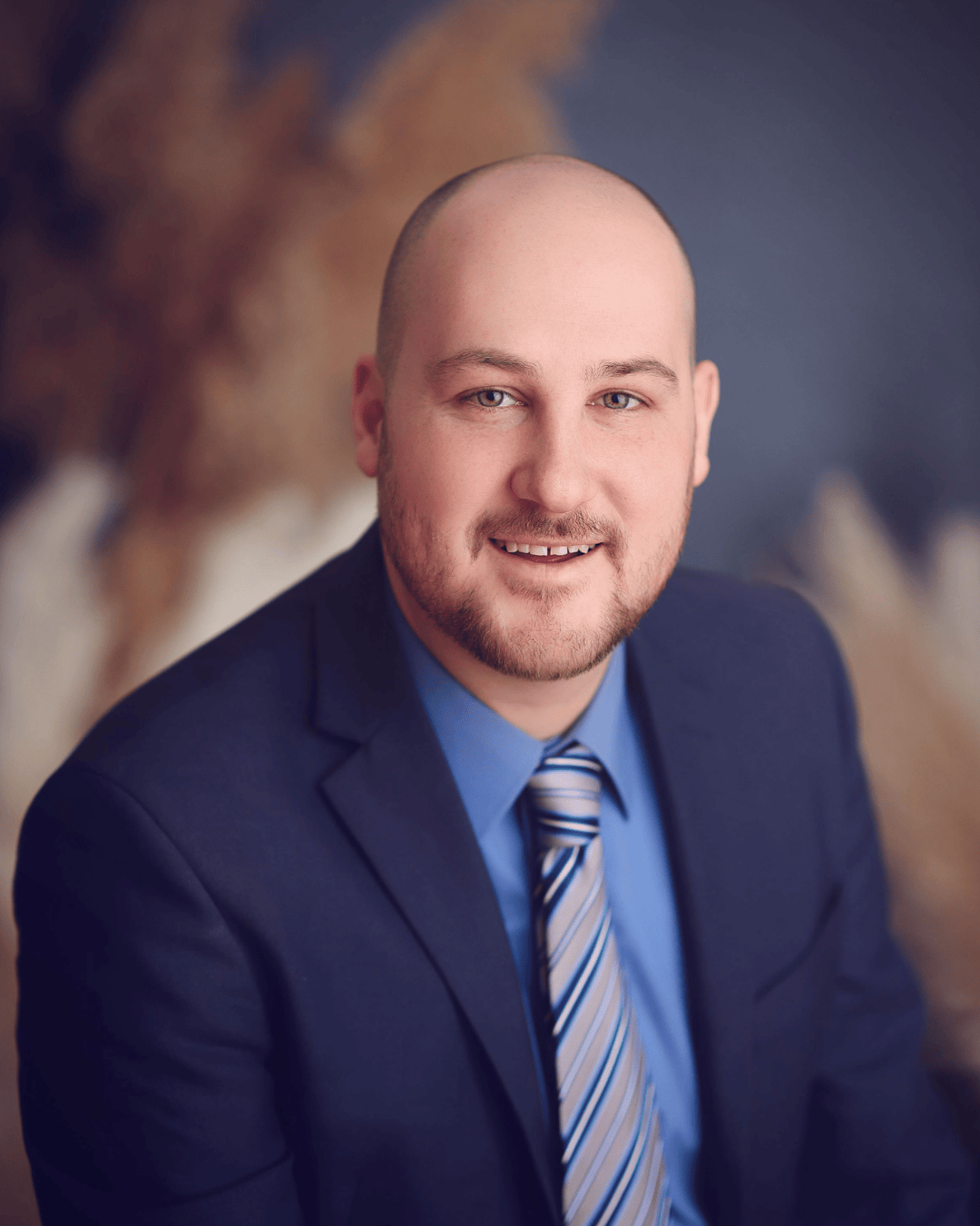 Portrait of a man in a blue suit, striped tie, with a blurred, colorful background.