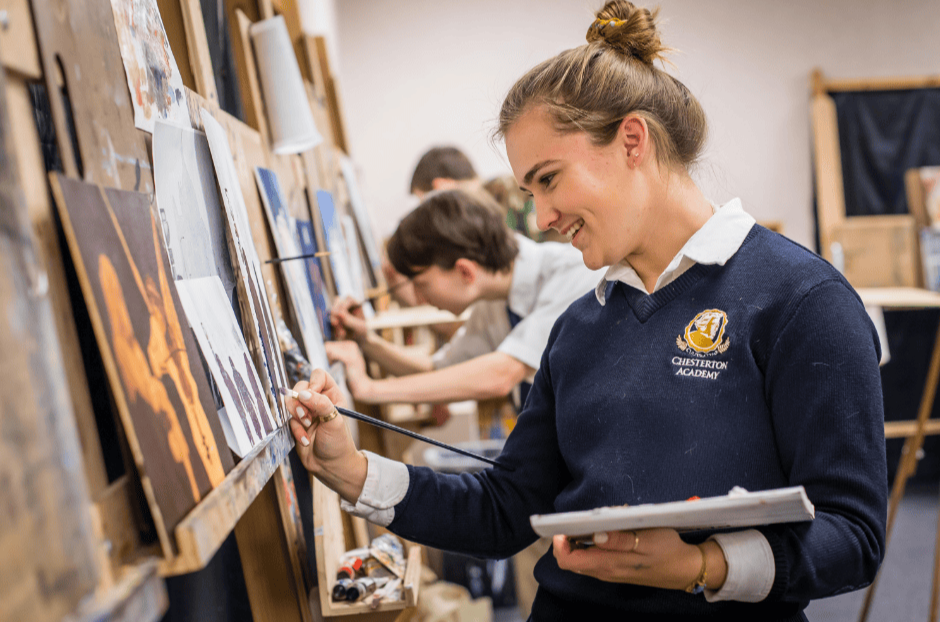 Young girl painting at an art studio with multiple students working on their canvases in the background.