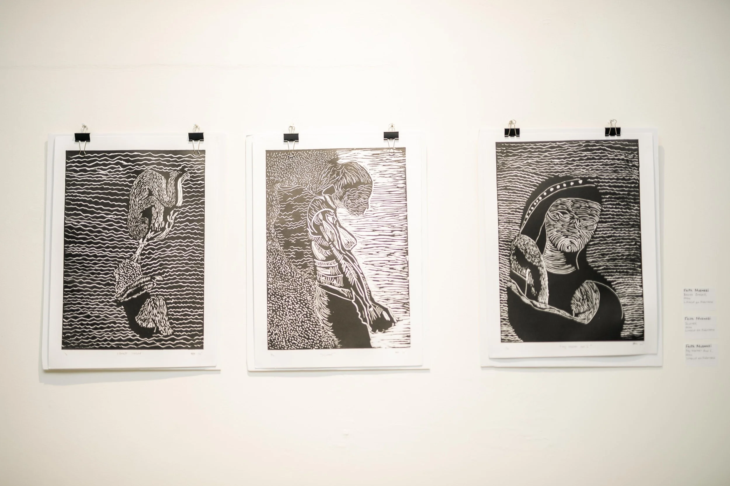 Three black and white art prints hanging on a white wall, each depicting an indigenous person with stylized lines and patterns.